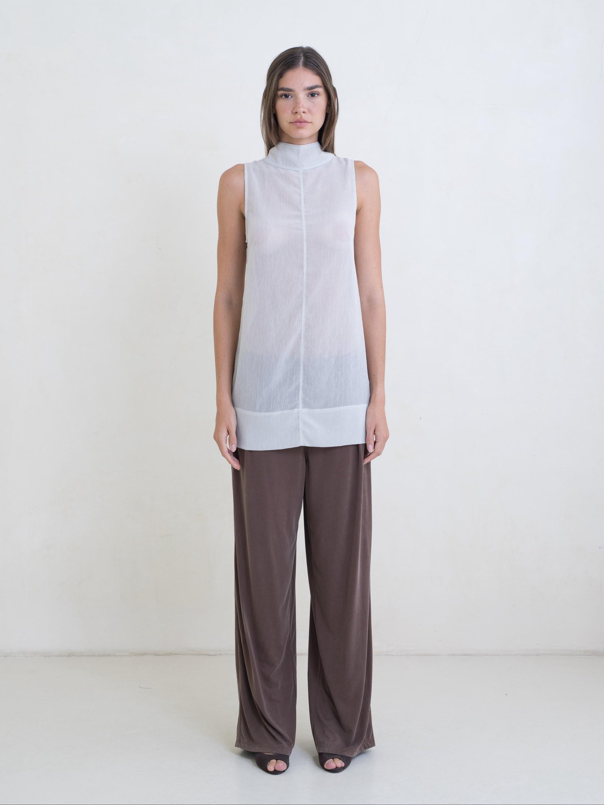 Woman wearing a sleeveless white top and brown pants on a white background
