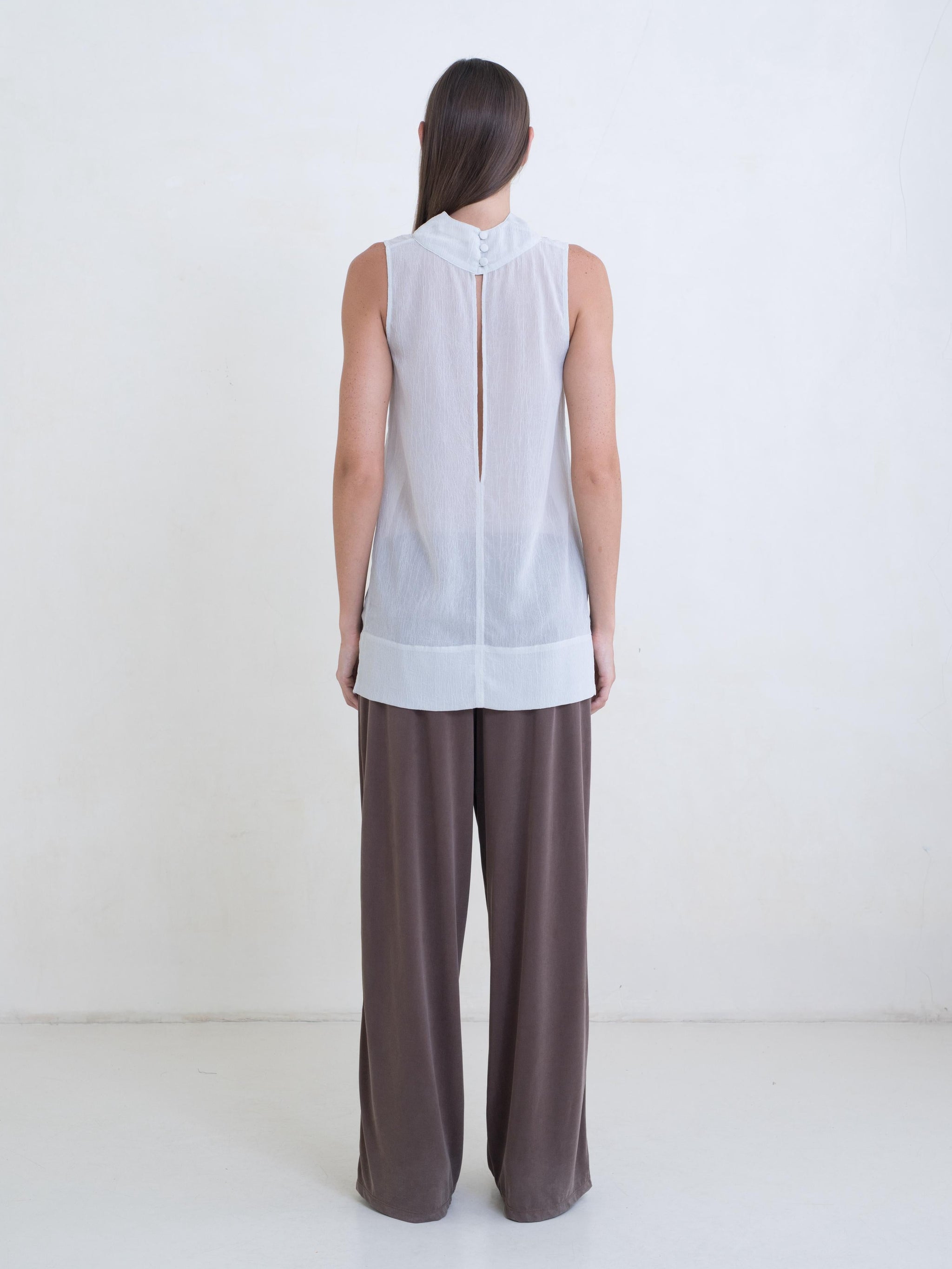 Woman wearing a sheer light green tunic and brown pants on a white background.