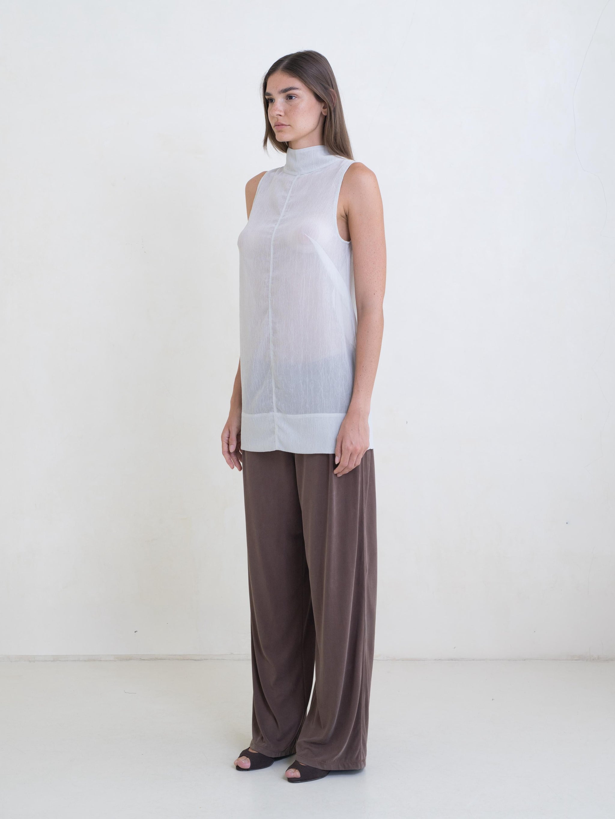 Woman wearing a sheer light green tunic and brown pants on a white background.