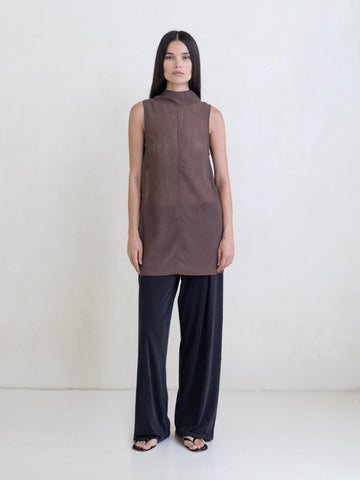Woman wearing a sheer brown sleeveless tunic and black pants on a white background.