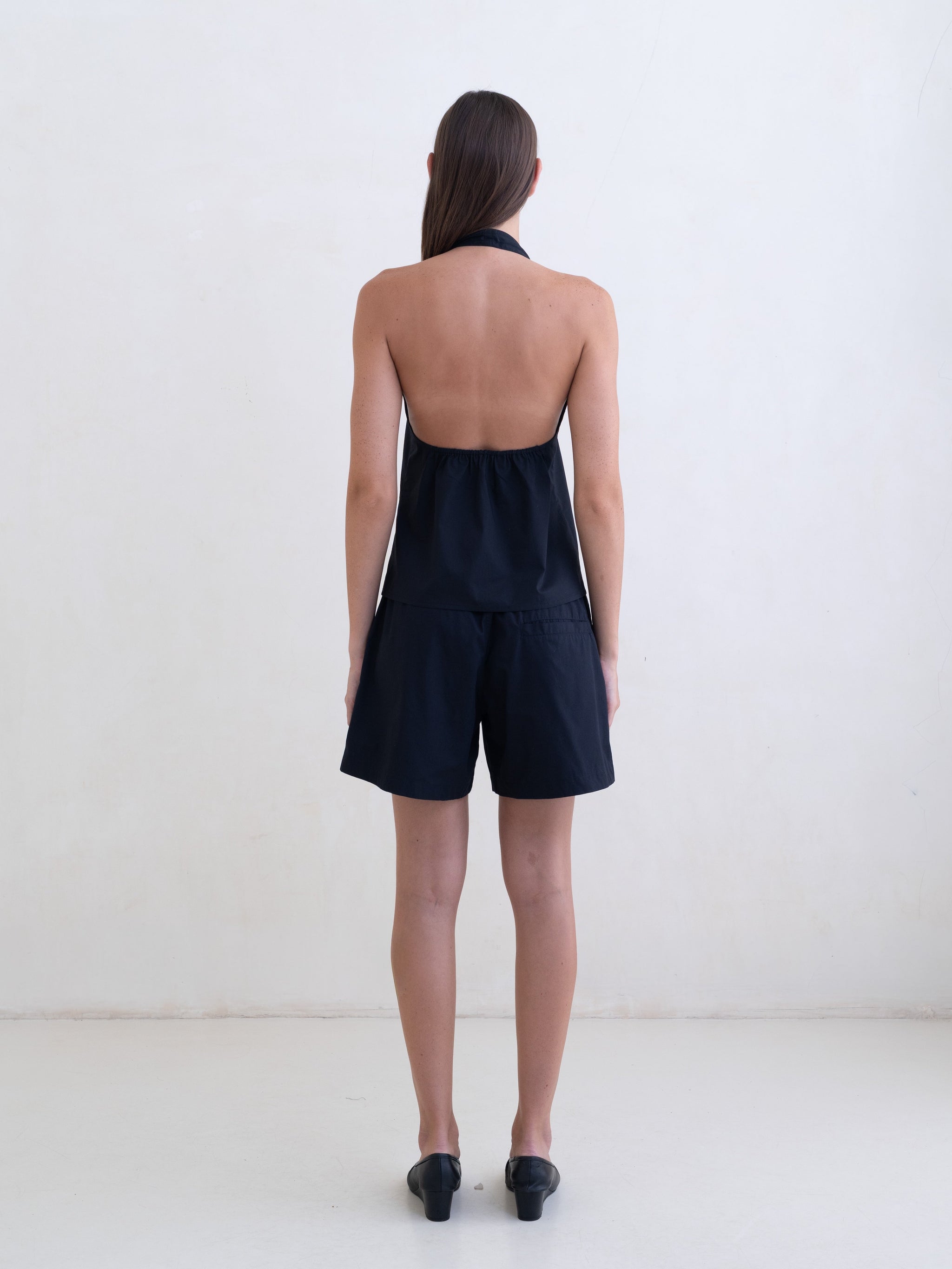 Woman wearing a black sleeveless halter neck top and black boxer shorts on a white background. 