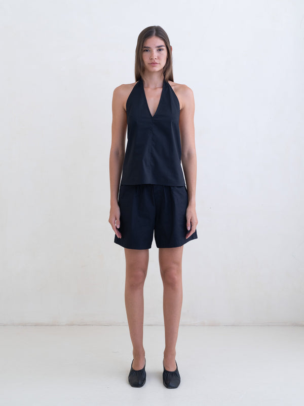 Woman wearing a black sleeveless halter neck top and black boxer shorts on a white background. 