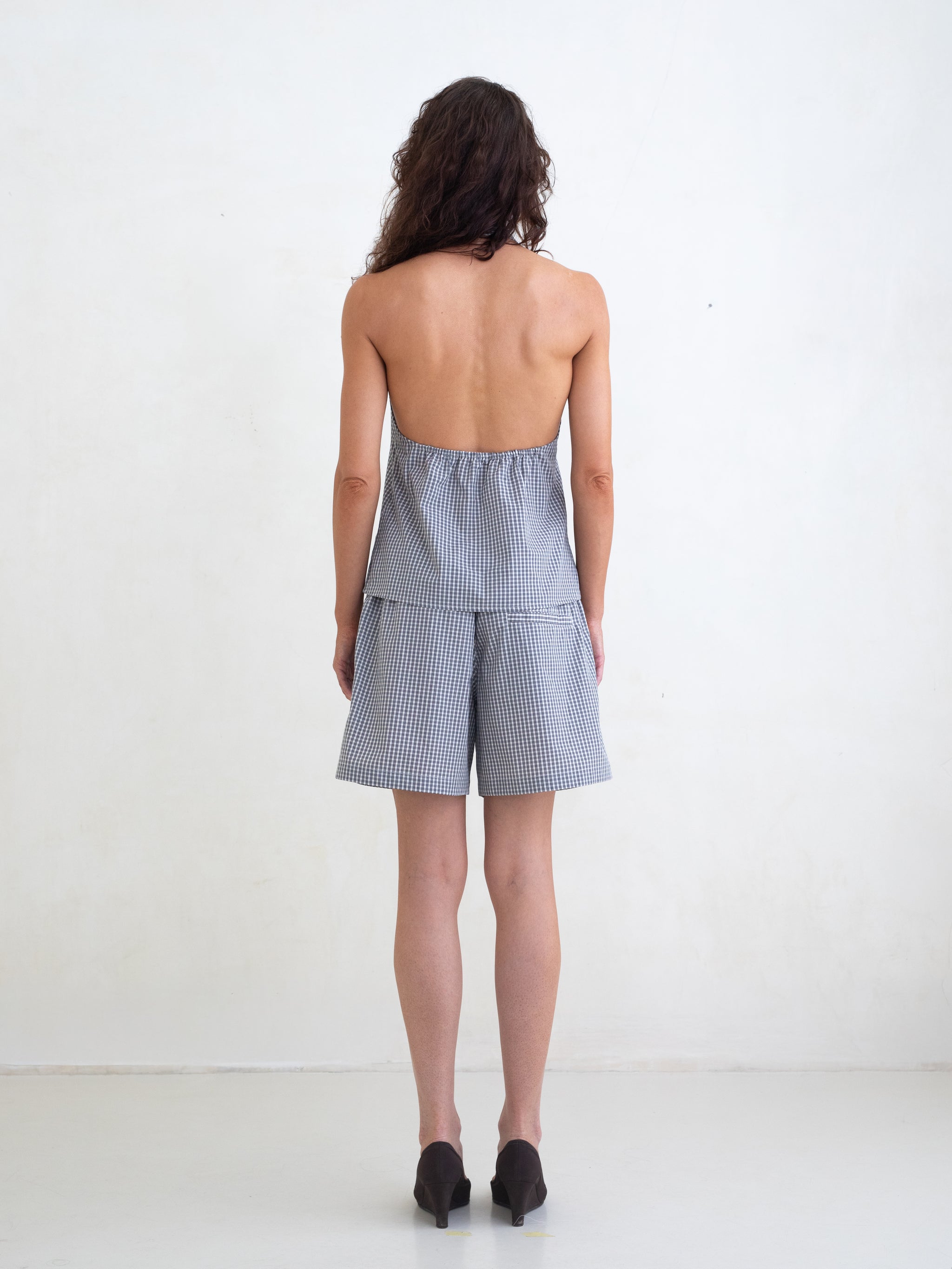 Woman wearing a black plaid v-neck halter top and matching black plaid boxer shorts on a white background. 