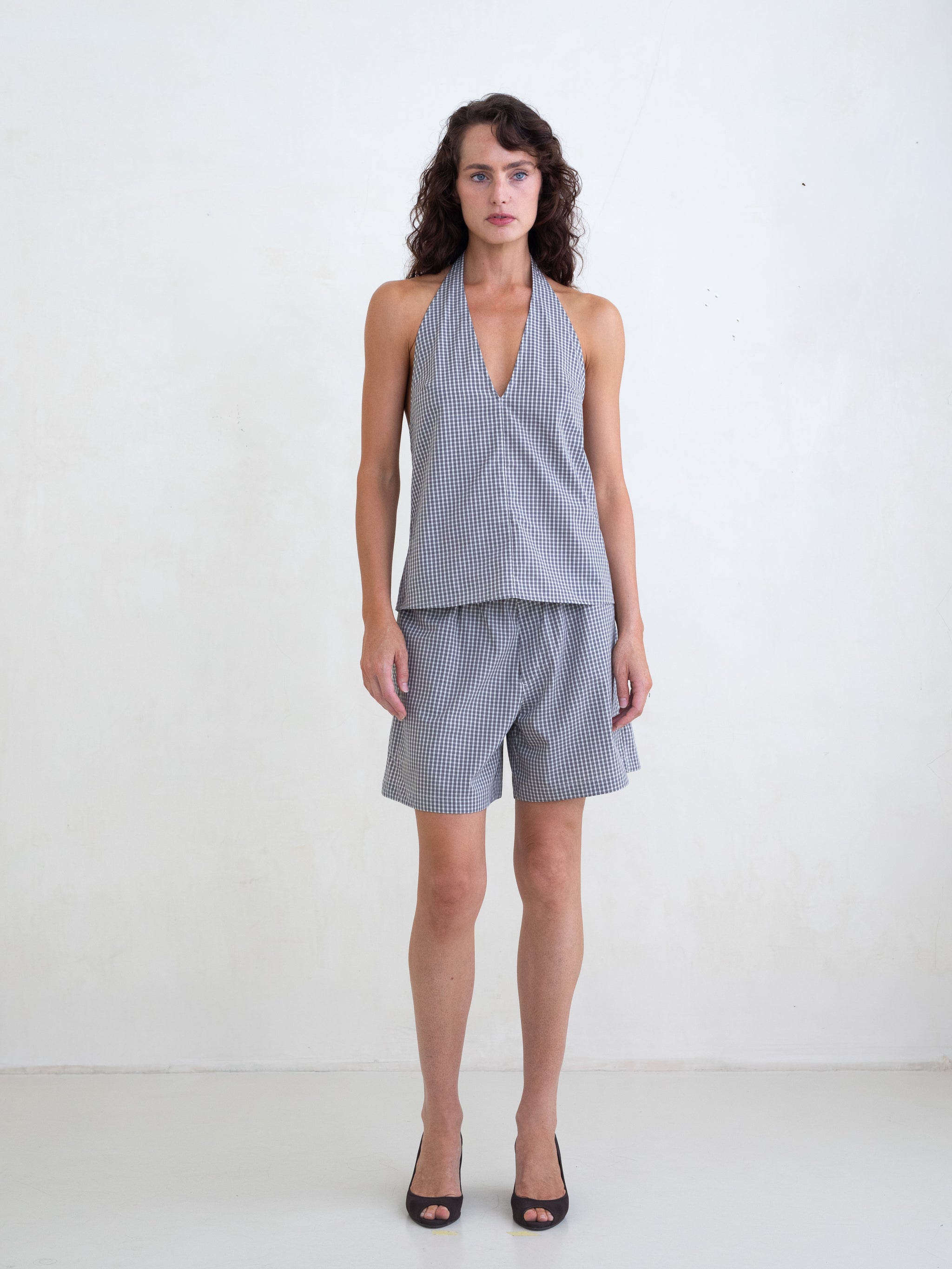 Woman wearing a black plaid v-neck halter top and matching black plaid boxer shorts on a white background. 