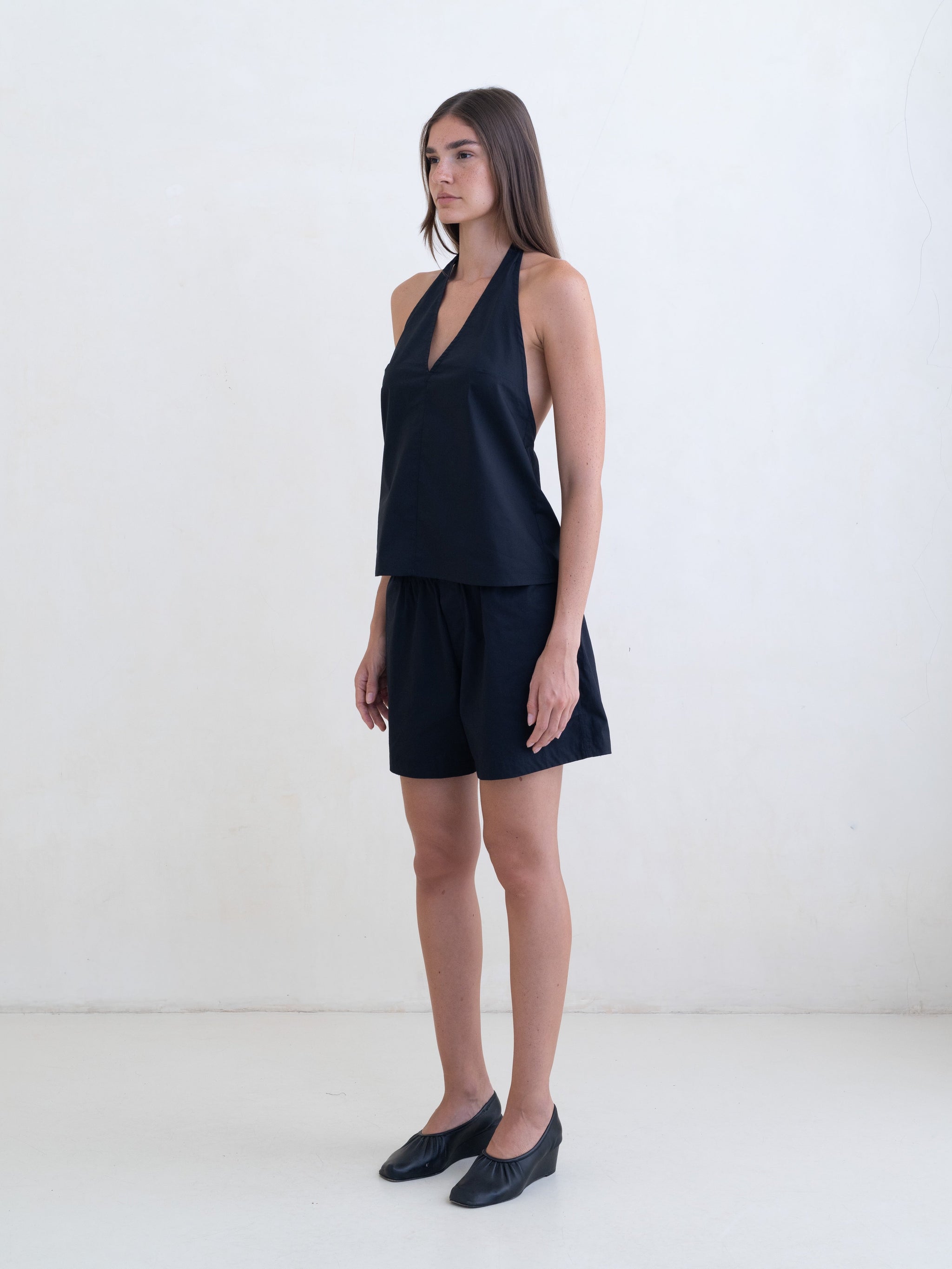 Woman wearing a black sleeveless halter neck top and black boxer shorts on a white background. 
