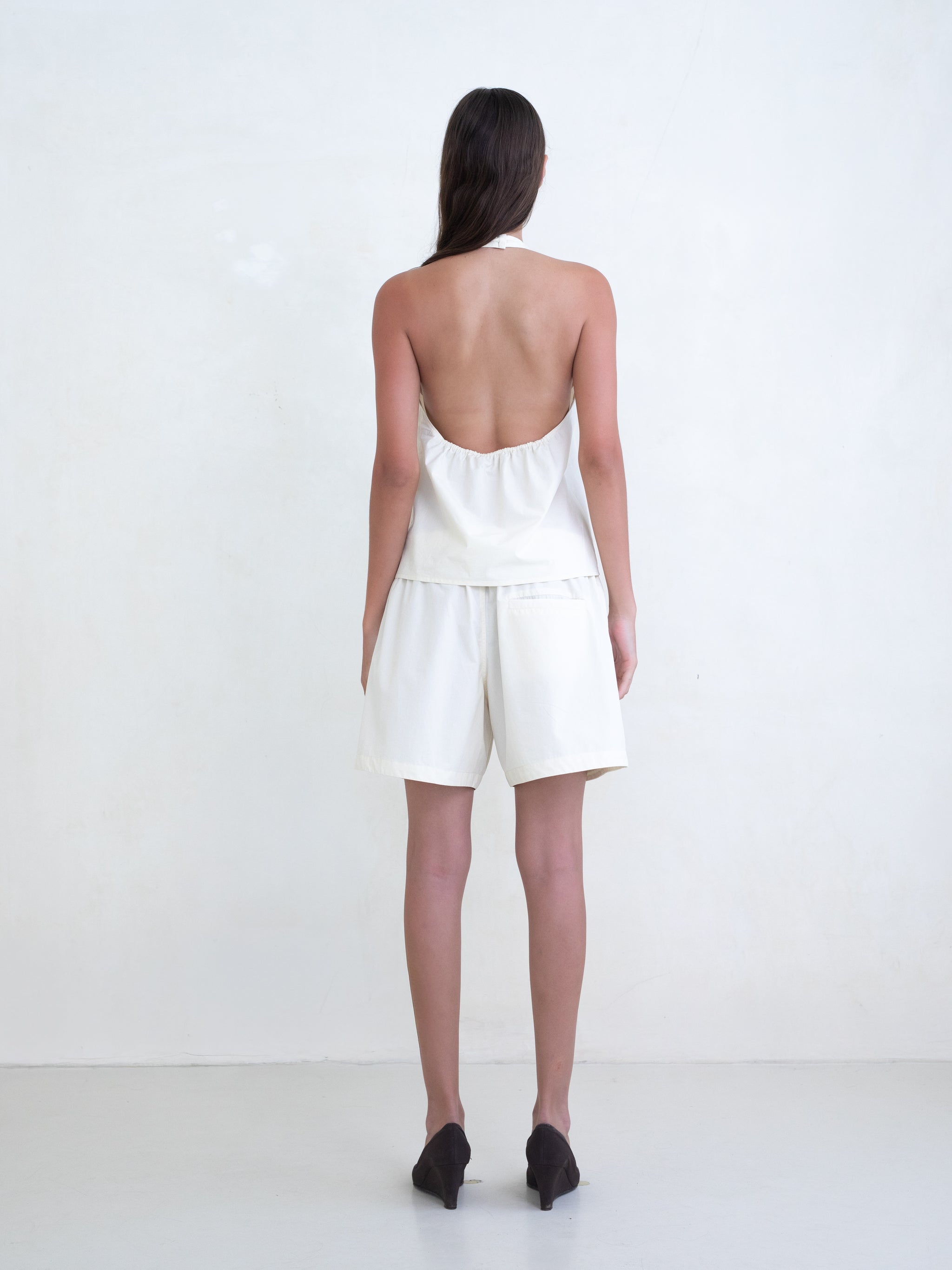 Woman wearing a cream v-neck halter top and matching cream boxer shorts on a white background. 