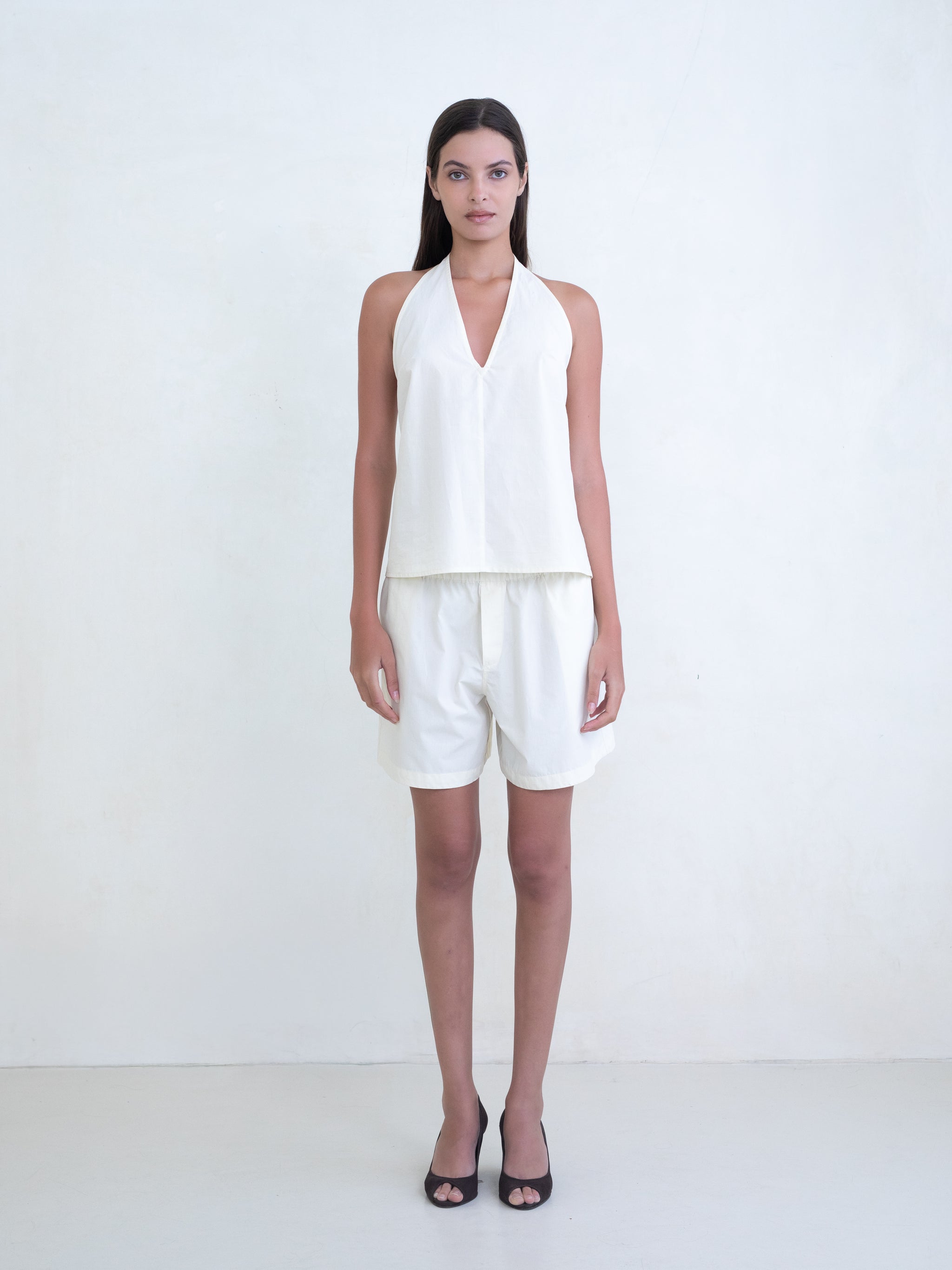Woman wearing a cream v-neck halter top and matching cream boxer shorts on a white background. 