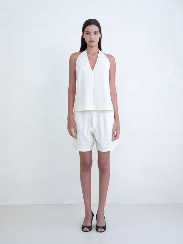 Woman wearing a cream v-neck halter top and matching cream boxer shorts on a white background. 