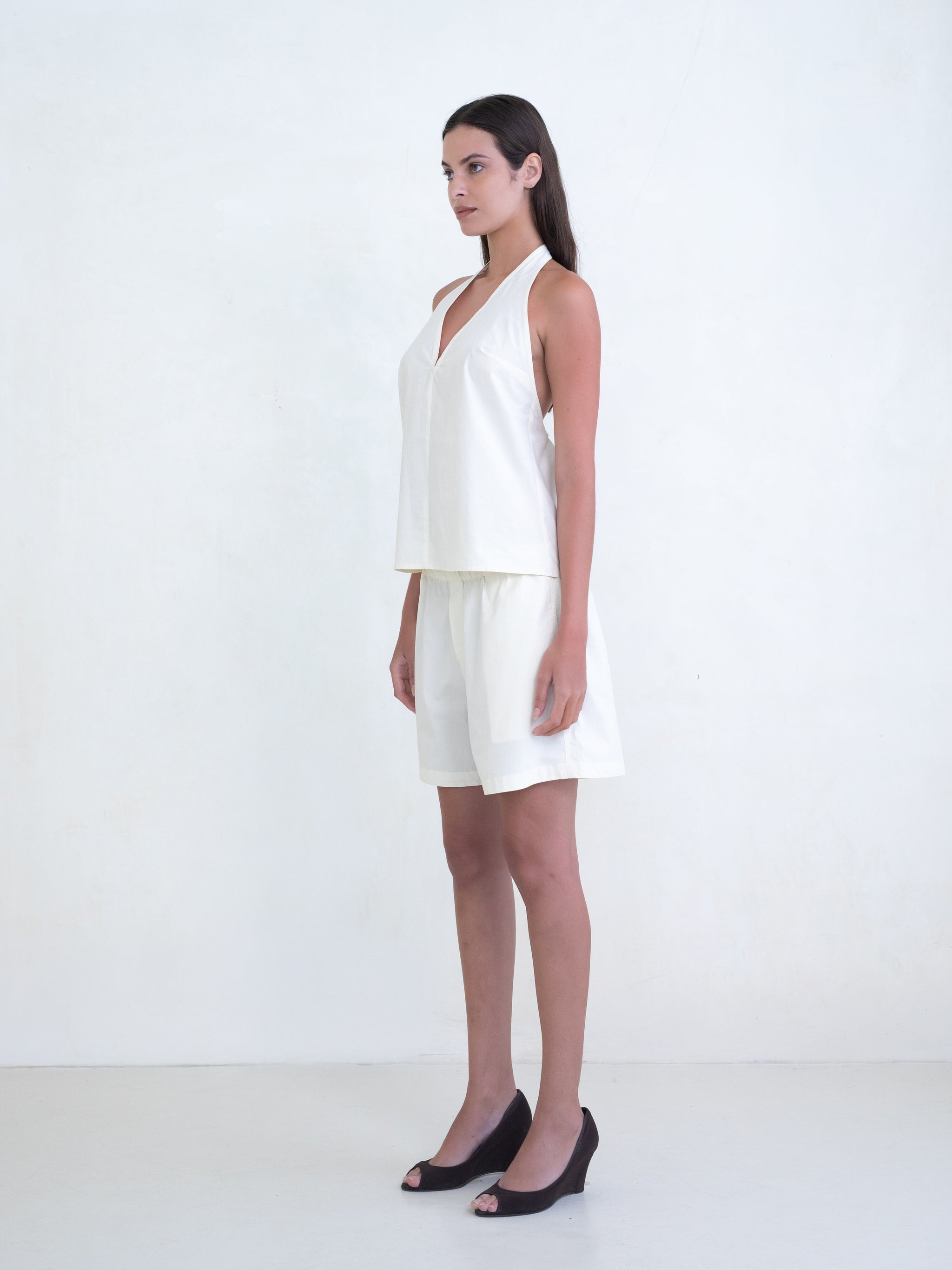 Woman wearing a cream v-neck halter top and matching cream boxer shorts on a white background. 