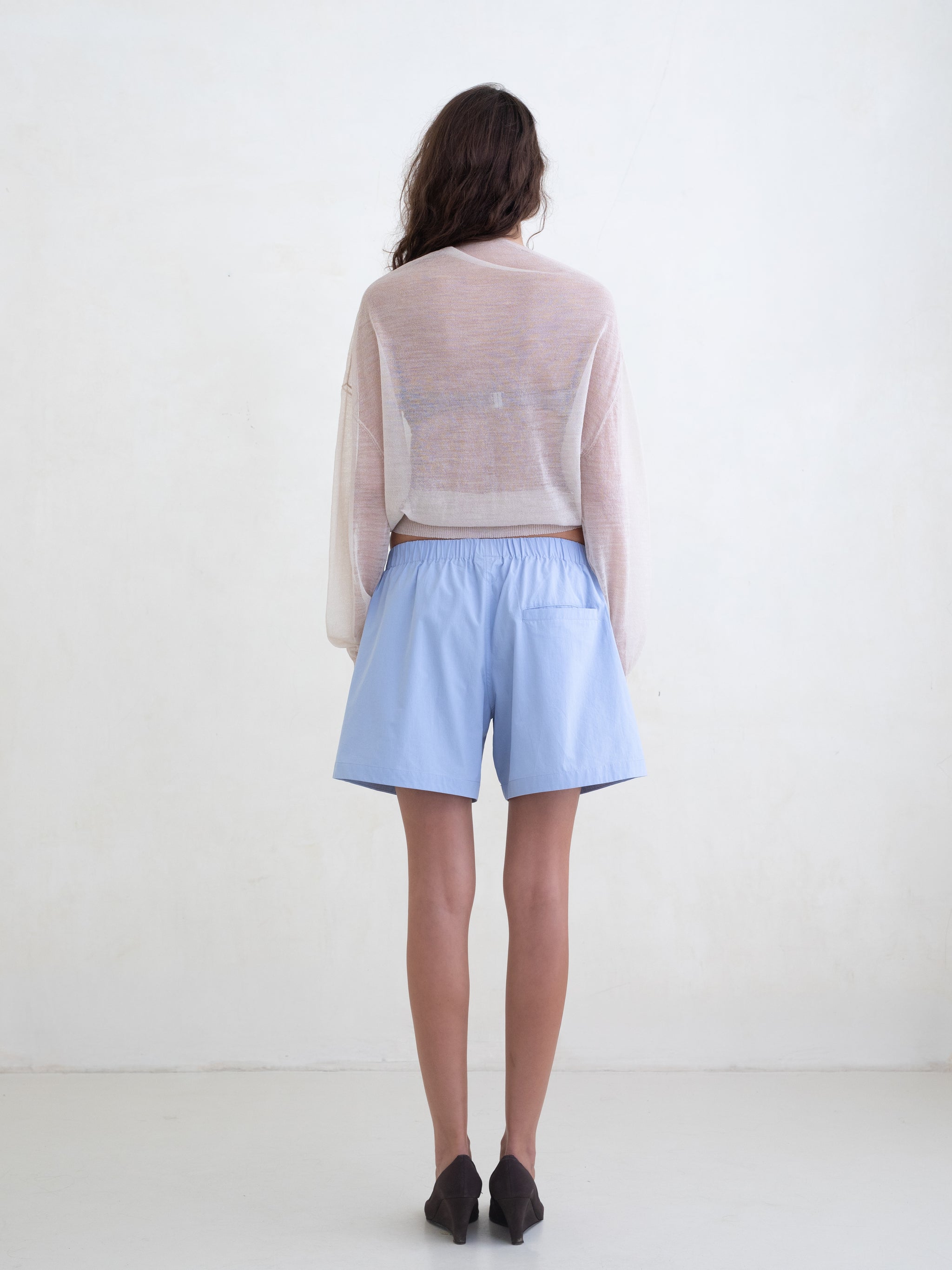 Woman wearing a sheer cream sweater and light blue boxer shorts on a white background. 
