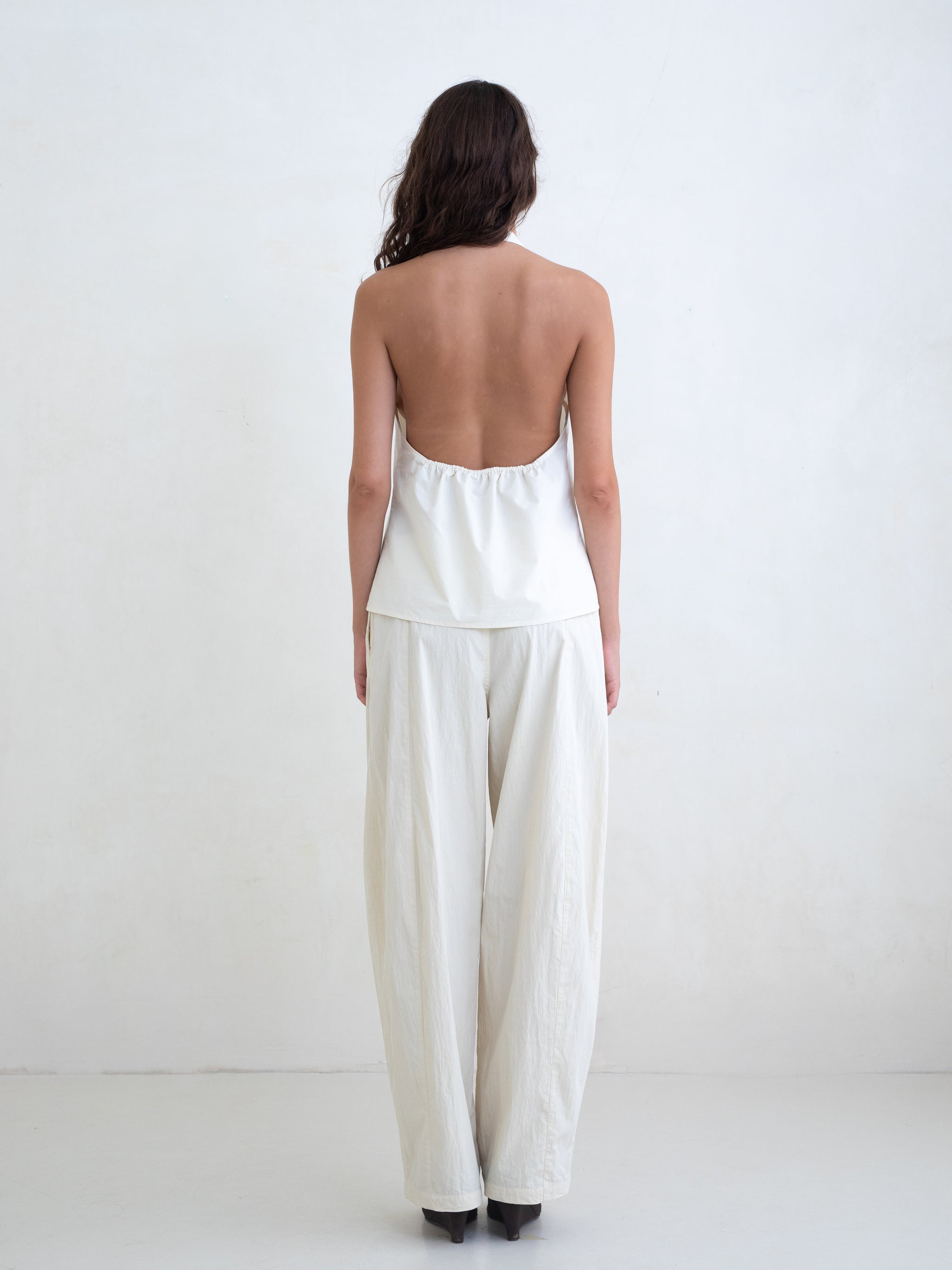 Woman wearing a cream v-neck halter top and cream straight leg trousers on a white background. 