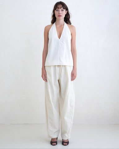 Woman wearing a cream v-neck halter top and cream straight leg trousers on a white background. 