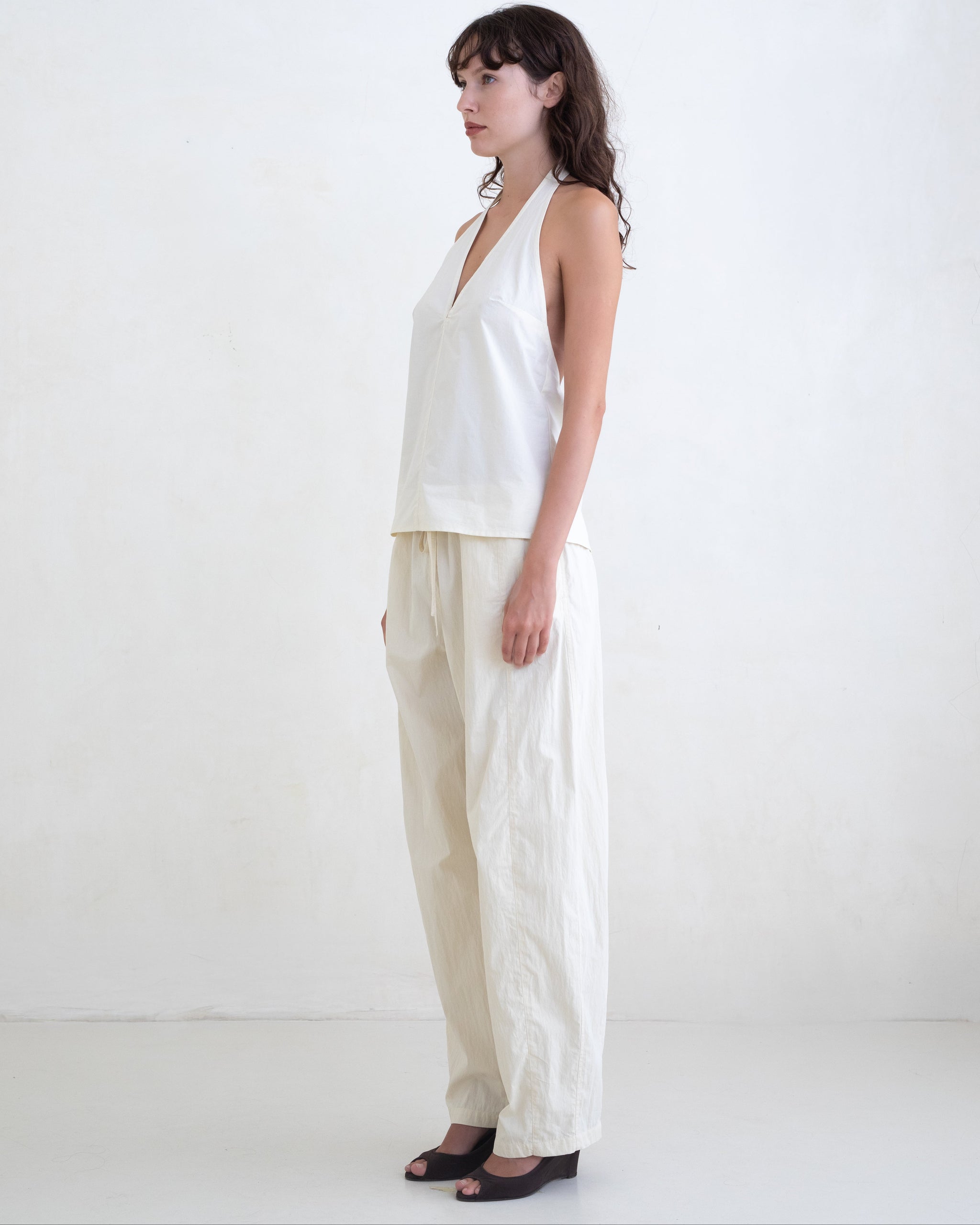 Woman wearing a cream v-neck halter top and cream straight leg trousers on a white background. 