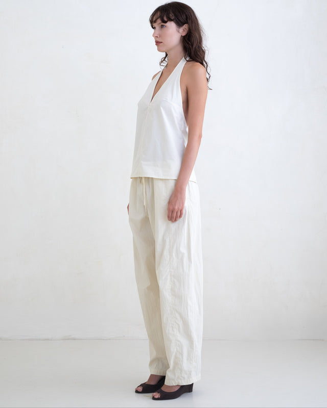 Woman wearing a cream v-neck halter top and cream straight leg trousers on a white background. 