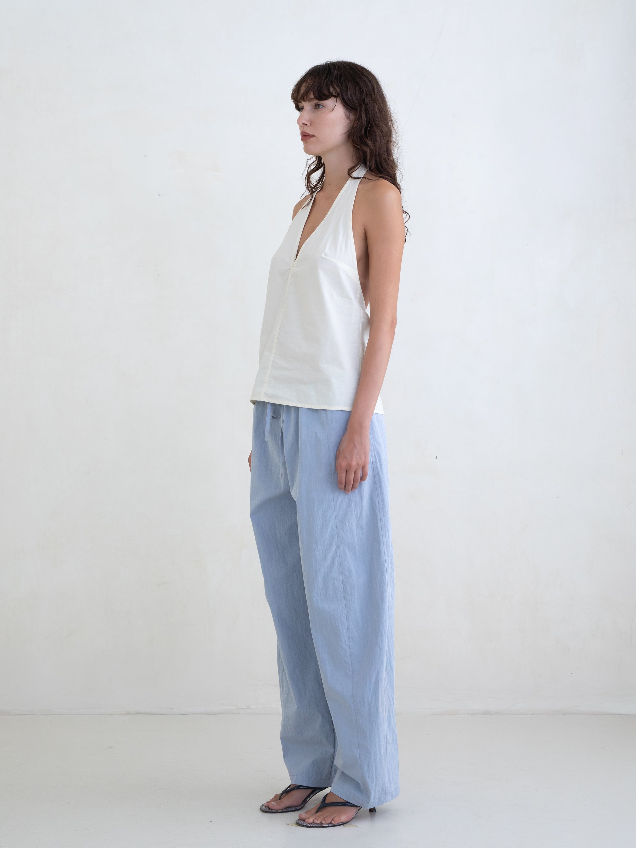 Woman wearing a cream v-neck halter top and light blue straight leg trousers on a white background. 