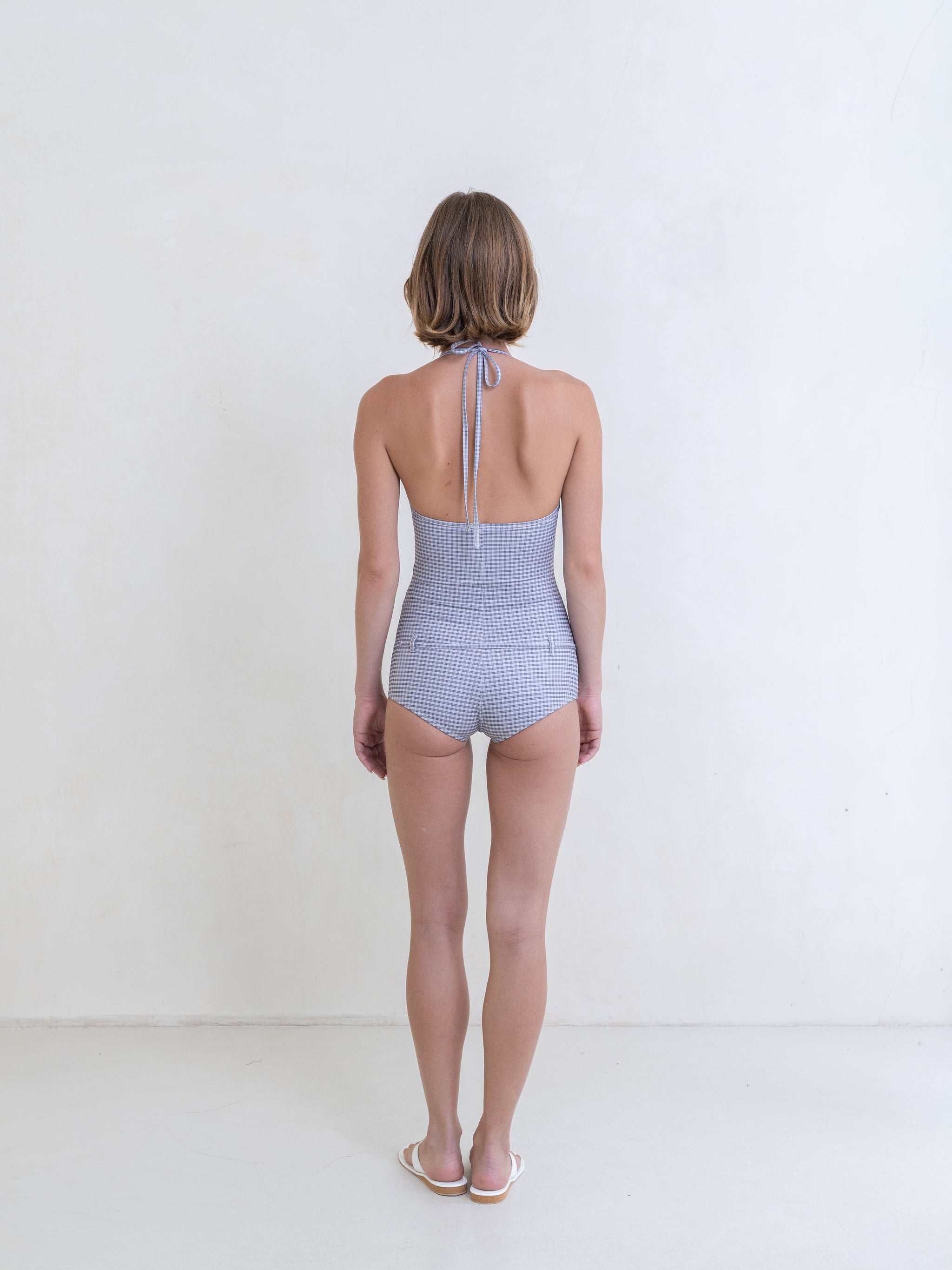 Woman wearing a gingham one-piece swimsuit on a white background.