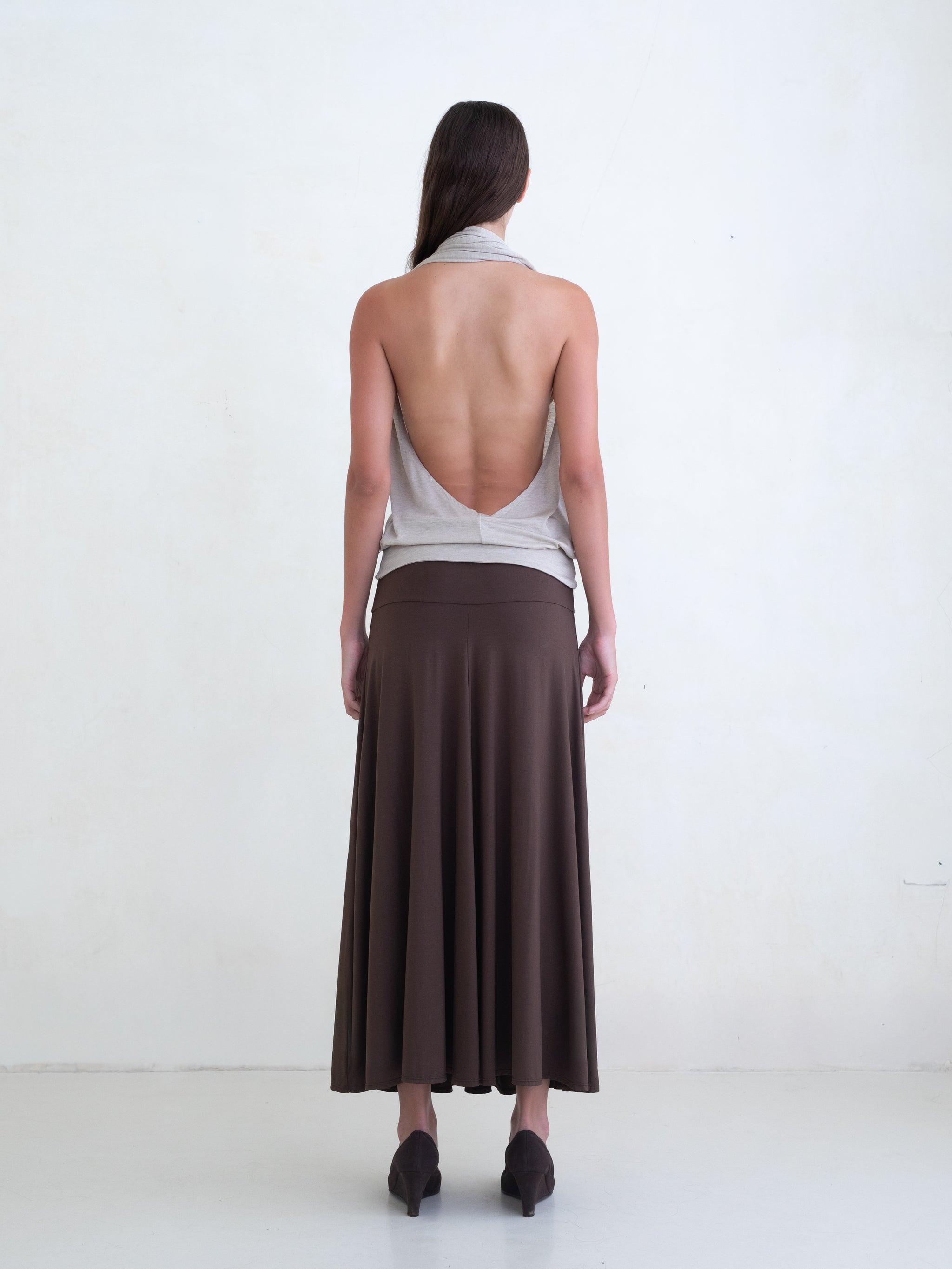 Woman wearing a beige draped halter top and a brown maxi skirt on a white background. 