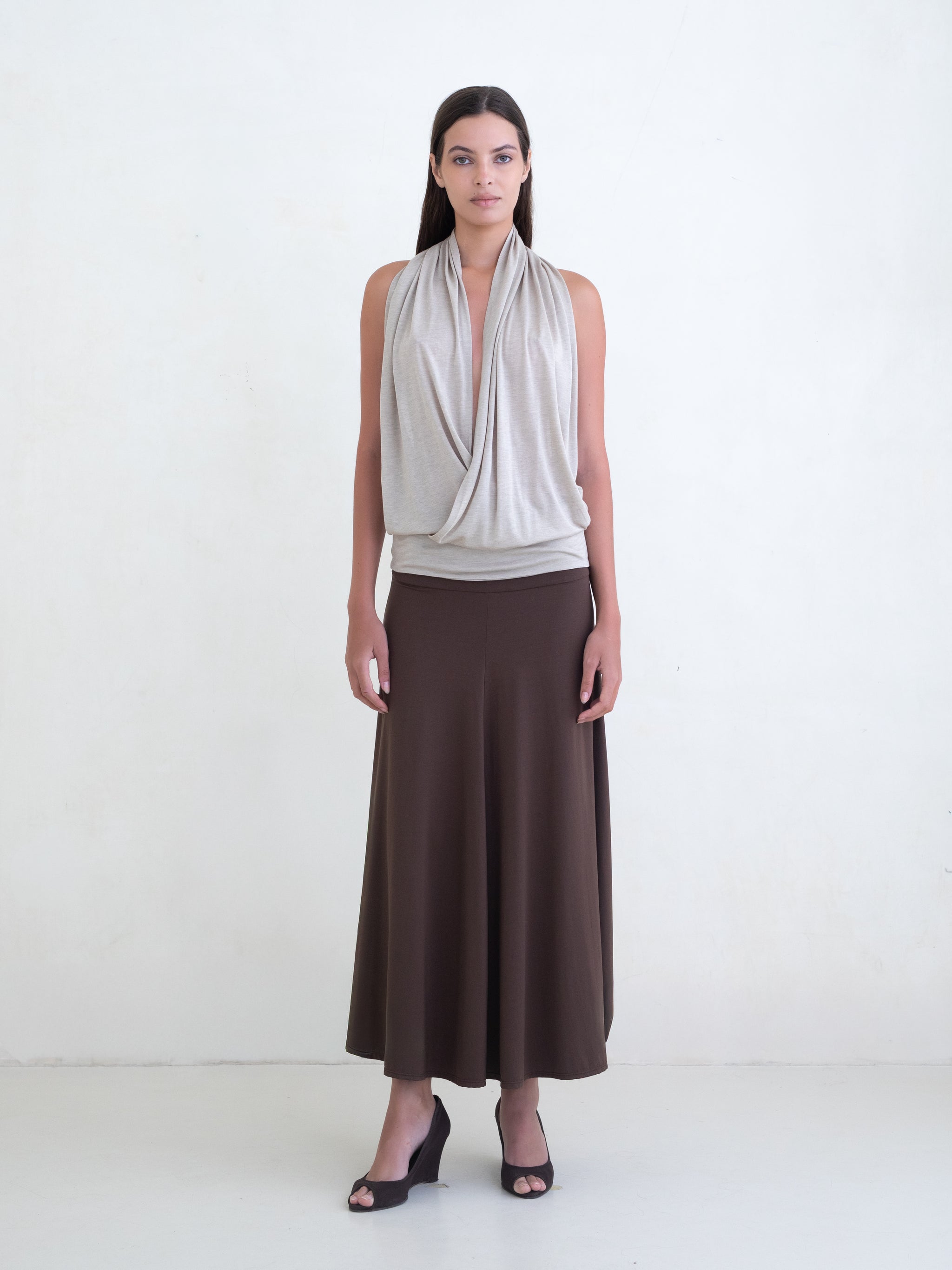 Woman wearing a beige draped halter top and a brown maxi skirt on a white background. 