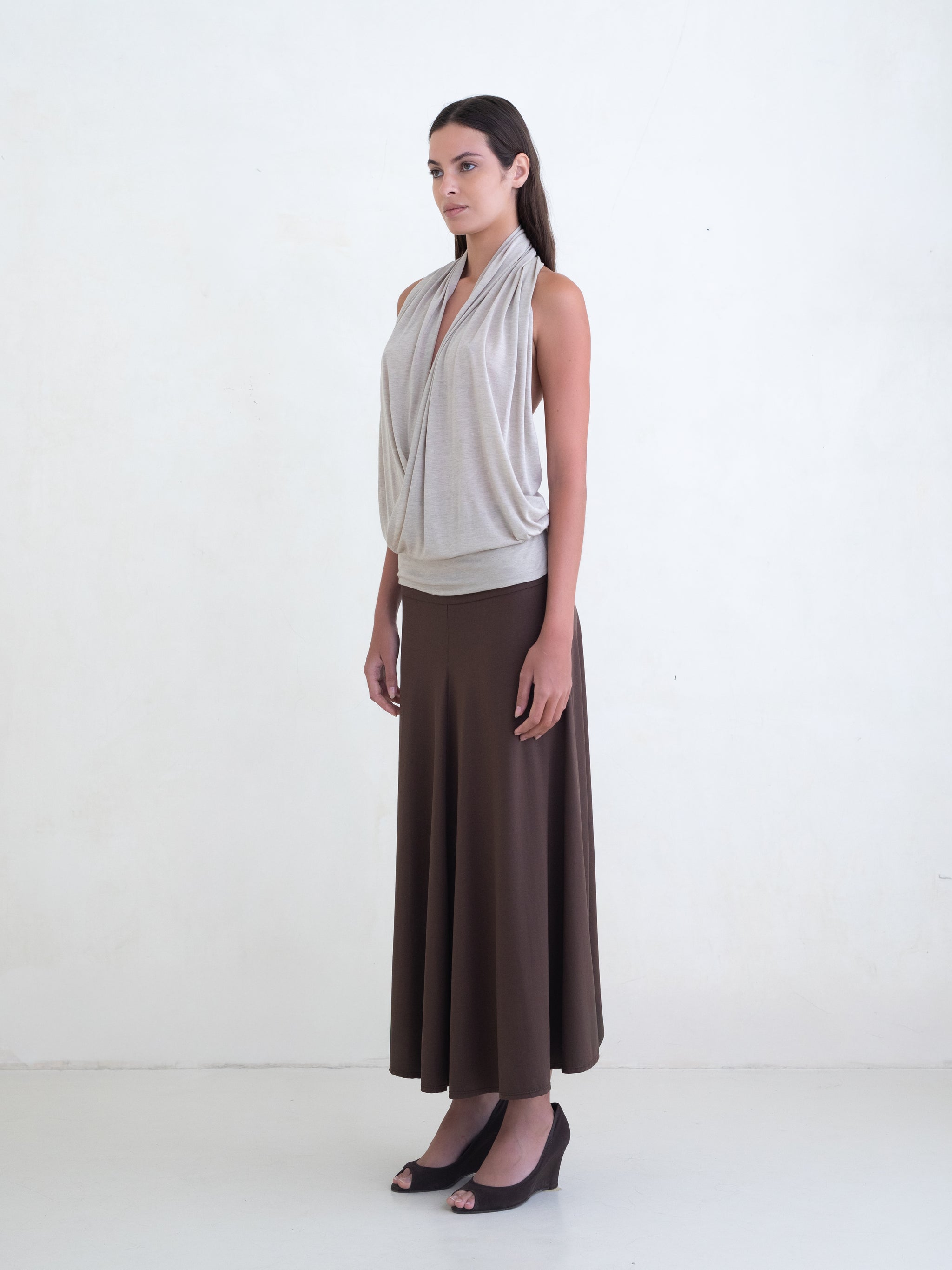 Woman wearing a beige draped halter top and a brown maxi skirt on a white background. 