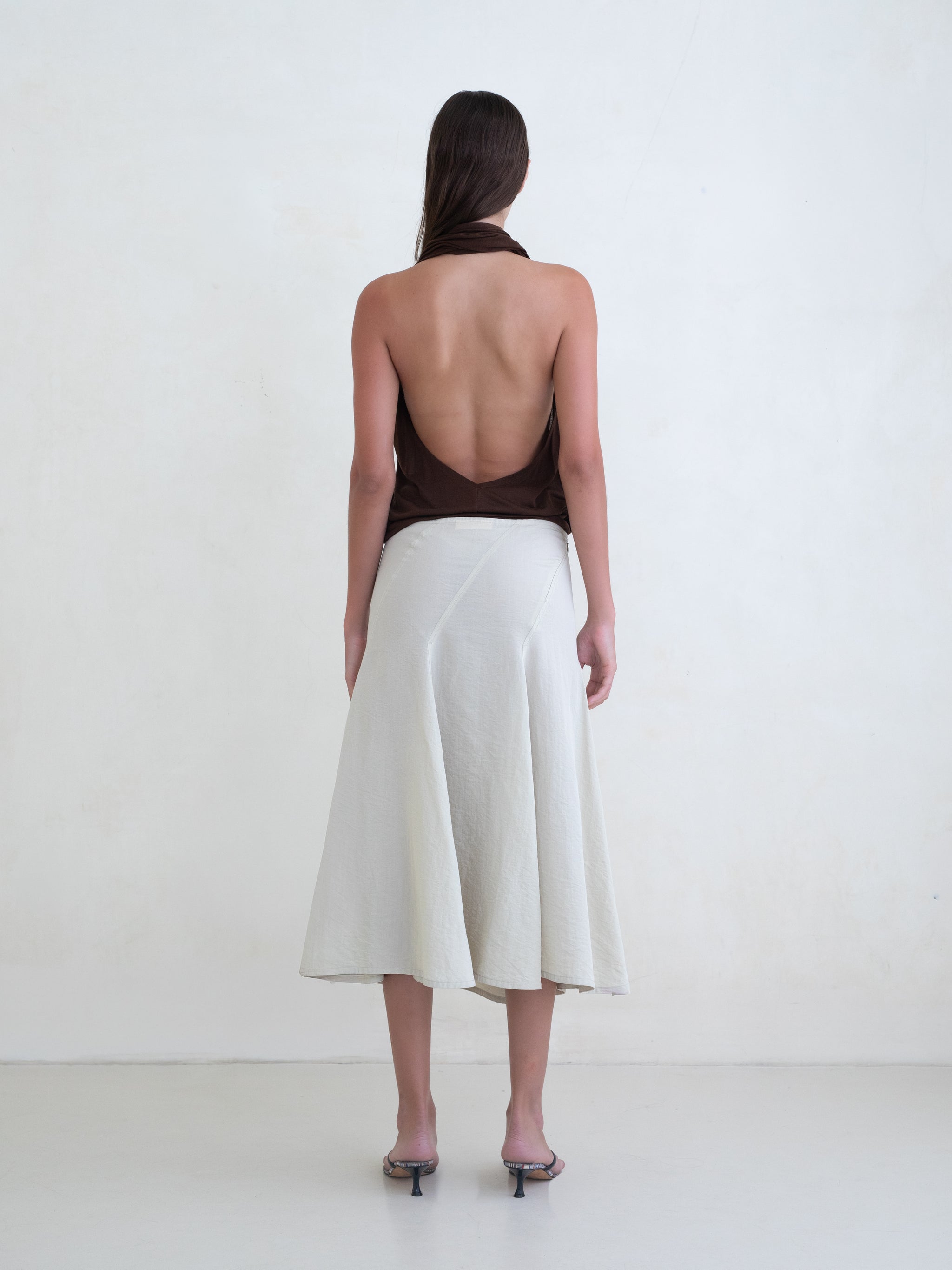 Woman wearing a brown draped halter top and a cream midi skirt on a white background. 