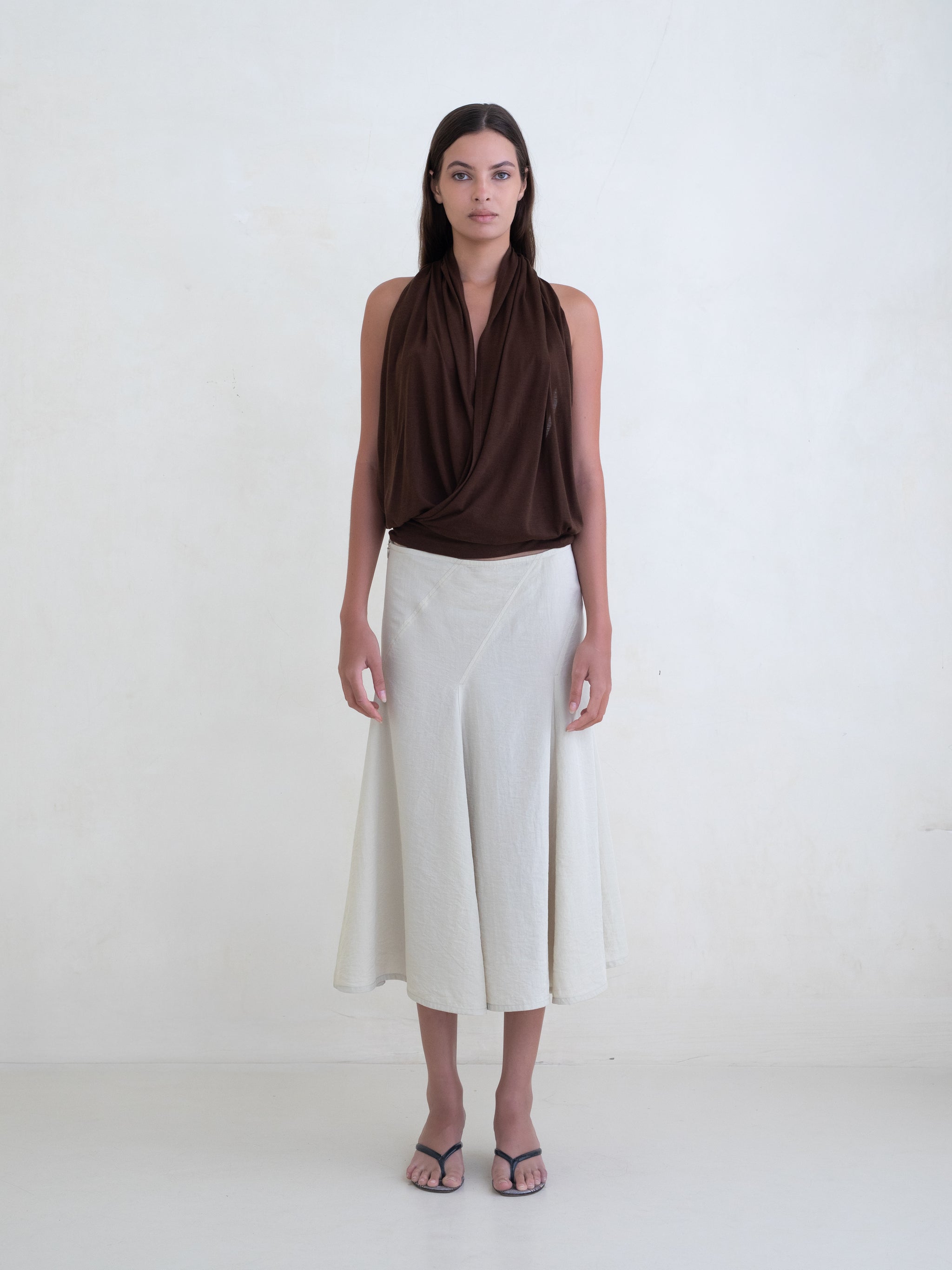 Woman wearing a brown draped halter top and a cream midi skirt on a white background. 
