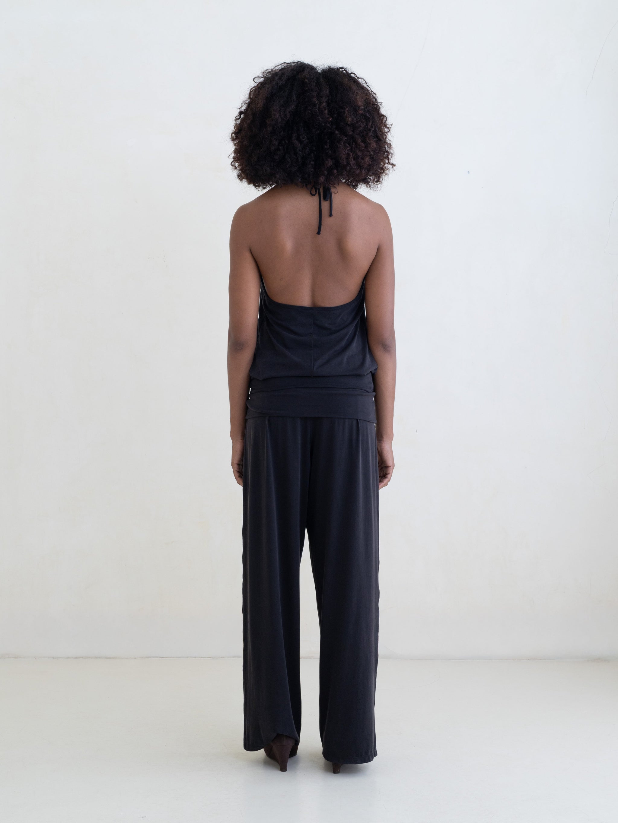 Woman wearing a black halter neck tank top and black straight leg pants on a white background. 