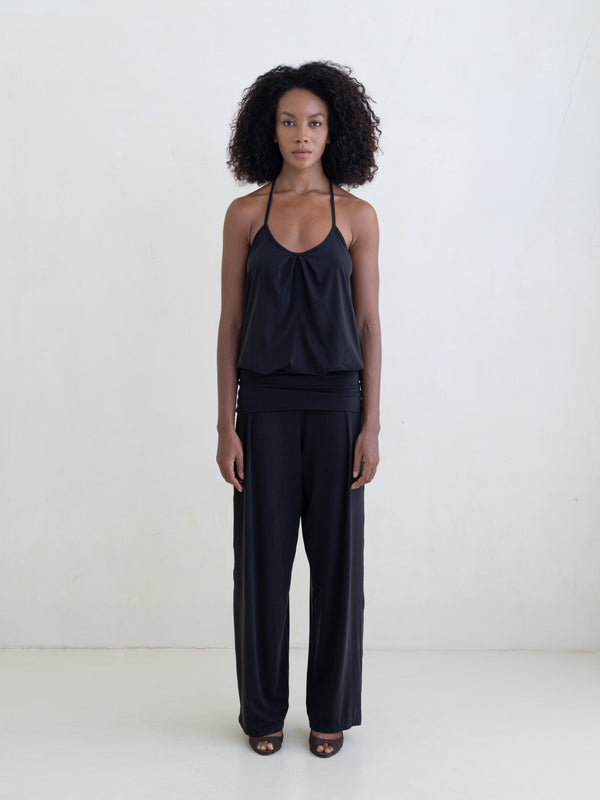 Woman wearing a black halter neck tank top and black straight leg pants on a white background. 