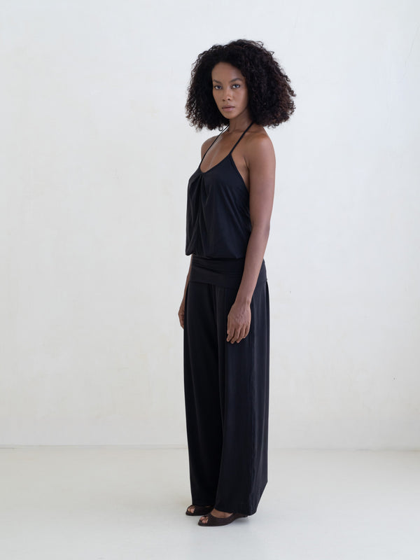 Woman wearing a black halter neck tank top and black straight leg pants on a white background. 