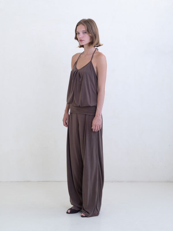 Woman wearing a brown halter neck tank top and brown straight leg pants on a white background. 