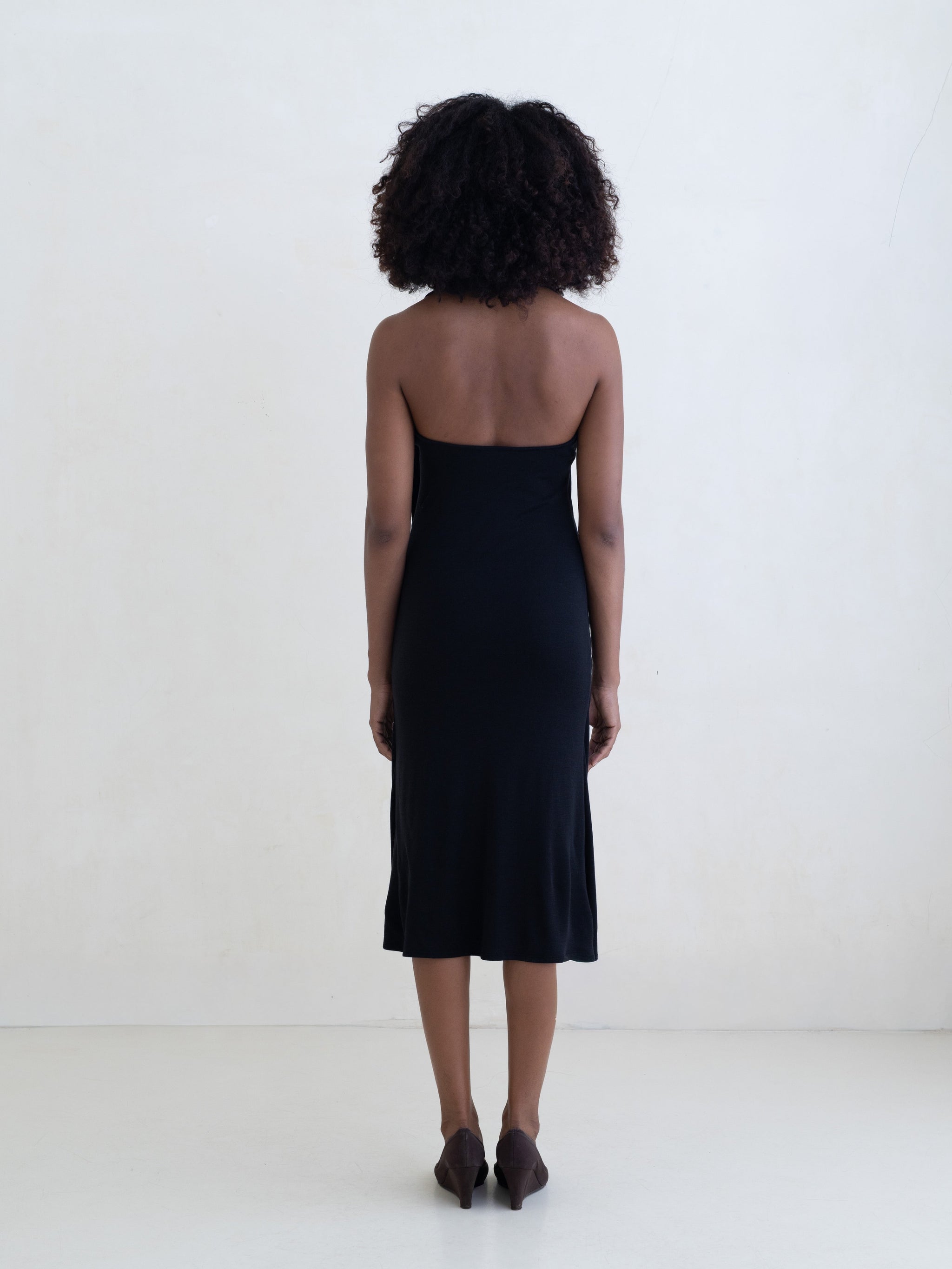 Woman wearing a black sleeveless V-neck midi dress on a white background.