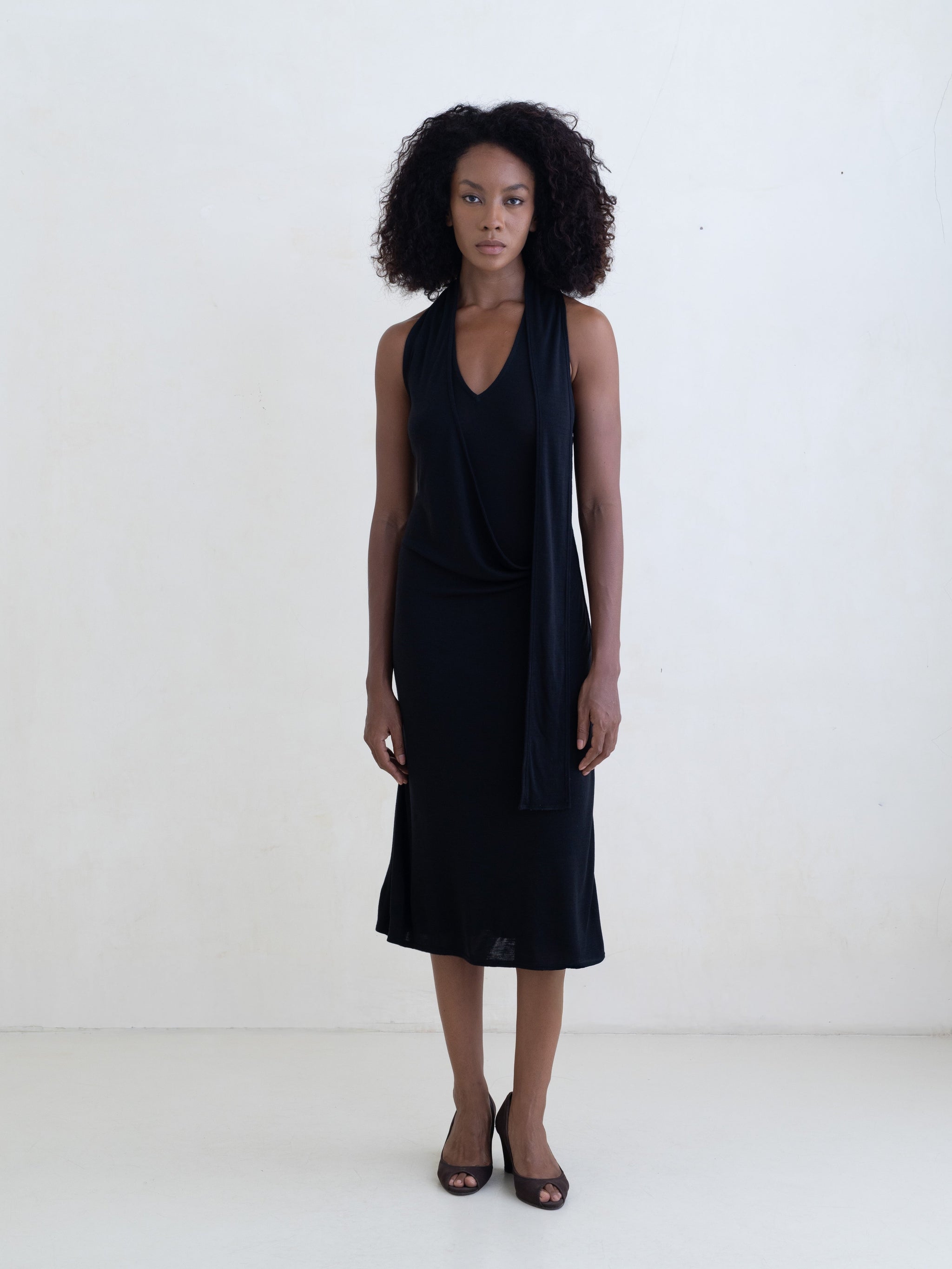 Woman wearing a black sleeveless V-neck midi dress on a white background.