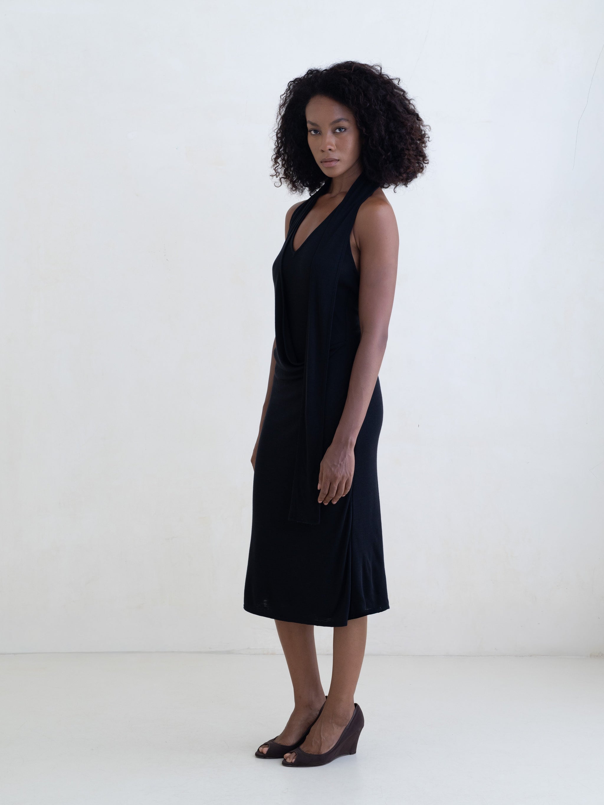 Woman wearing a black sleeveless V-neck midi dress on a white background.