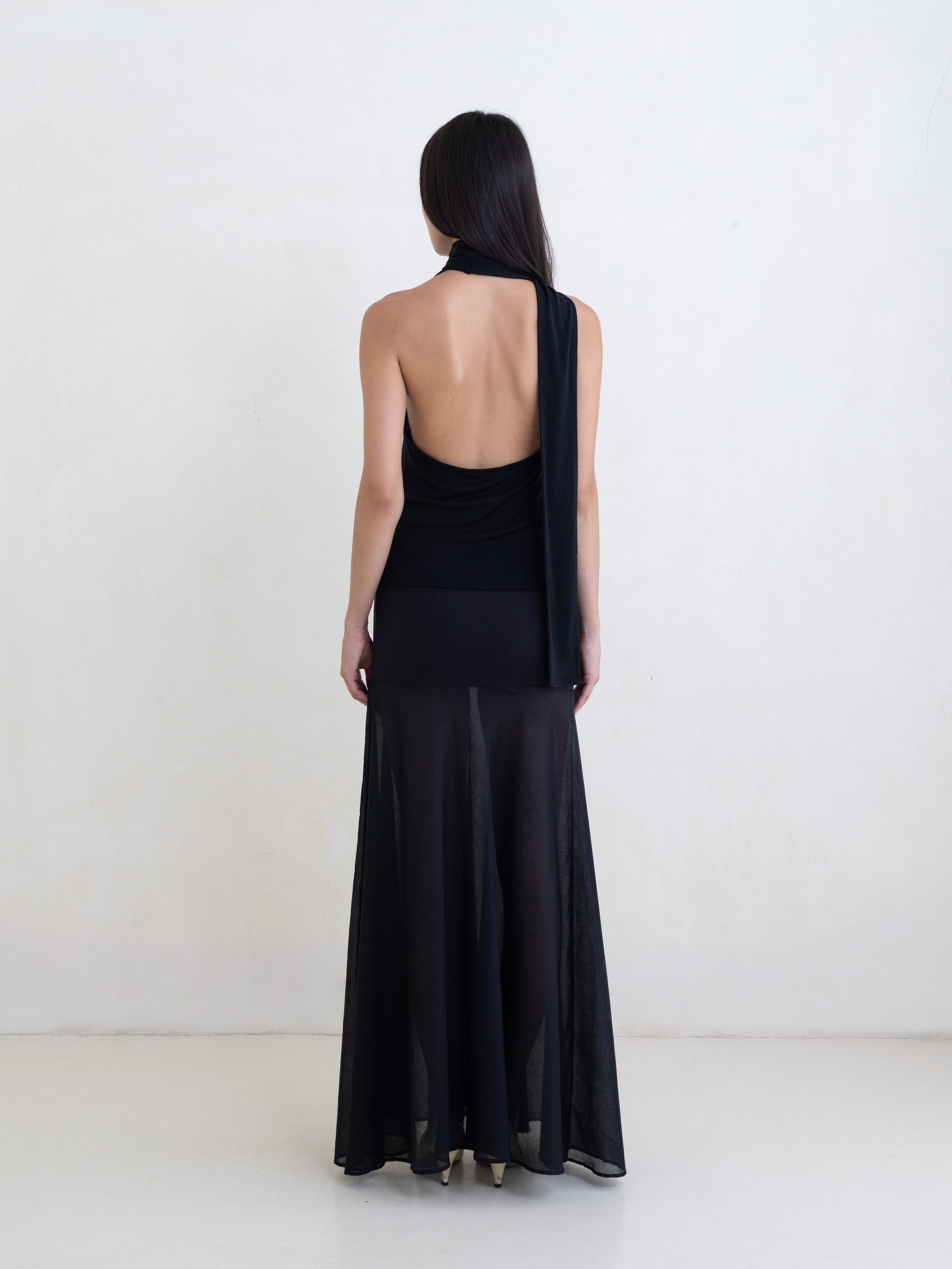 Woman wearing a black sleeveless halter-style wrap top and a black maxi skirt on a white background. 