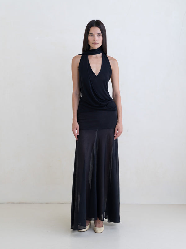 Woman wearing a black sleeveless halter-style wrap top and a black maxi skirt on a white background. 