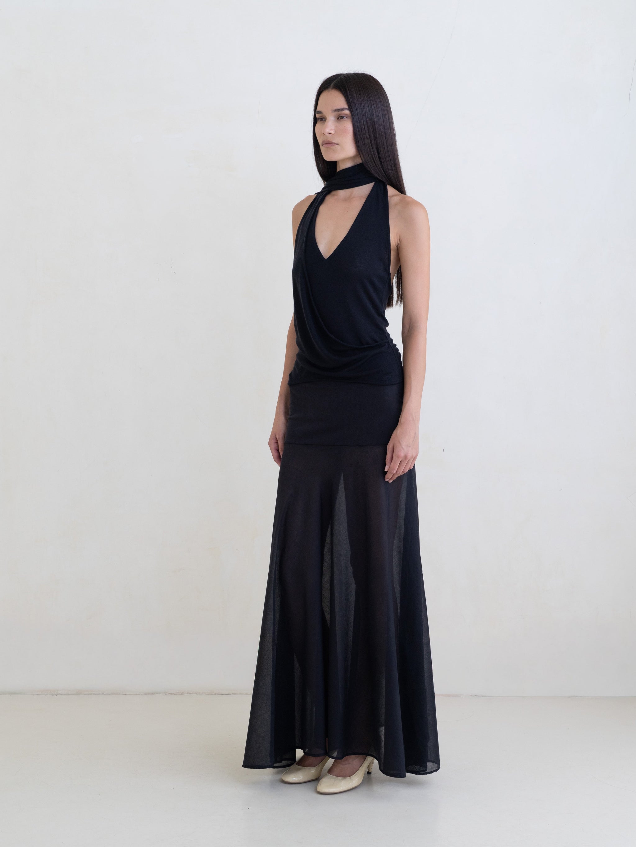 Woman wearing a black sleeveless halter-style wrap top and a black maxi skirt on a white background. 