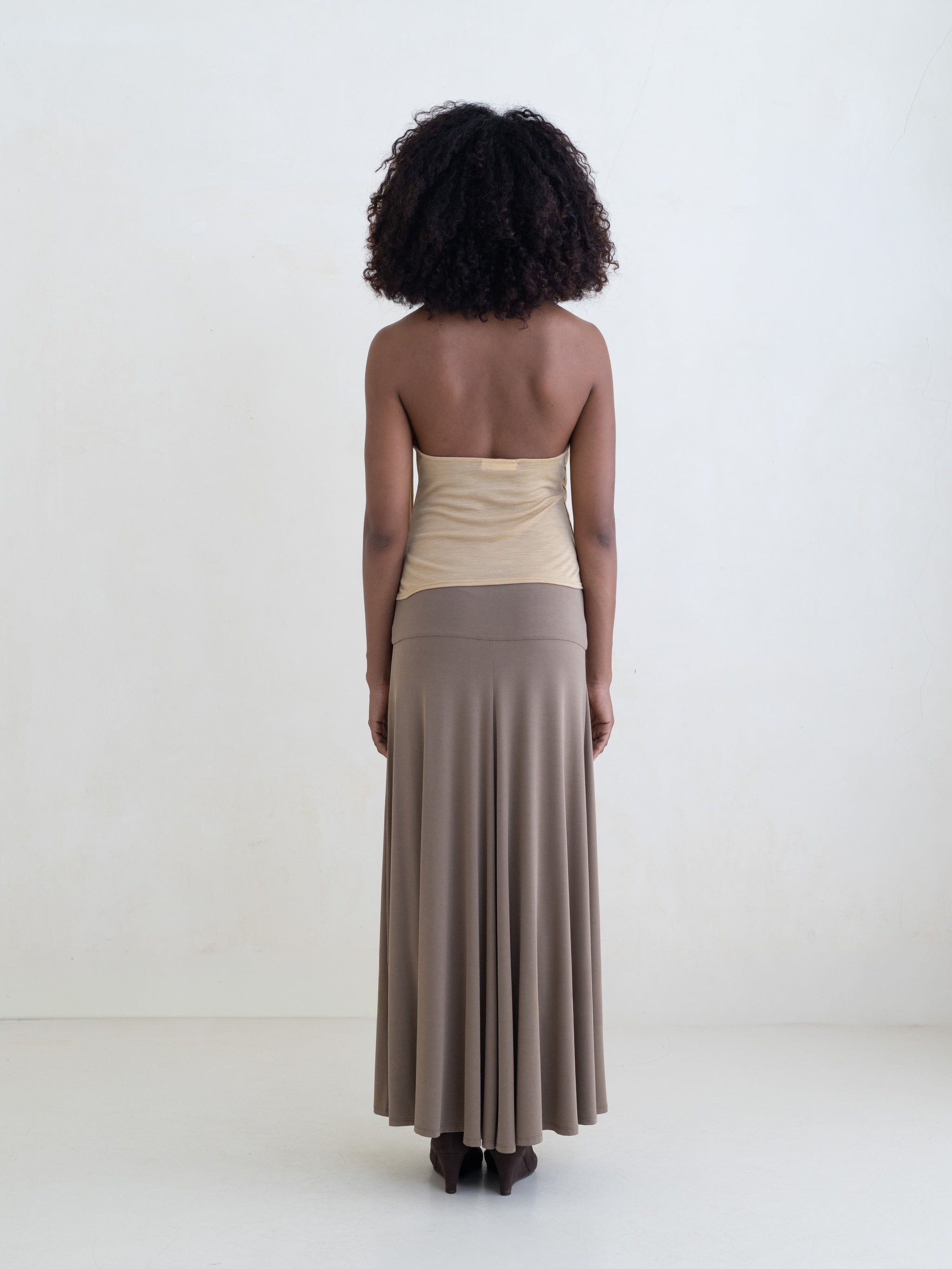 Woman wearing a light yellow sleeveless halter-style wrap top and a taupe maxi skirt on a white background. 