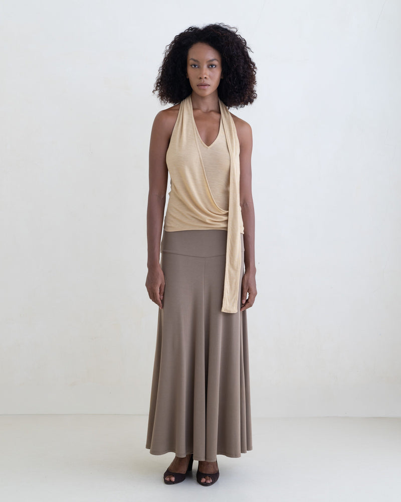 Woman wearing a light yellow sleeveless halter-style wrap top and a taupe maxi skirt on a white background. 