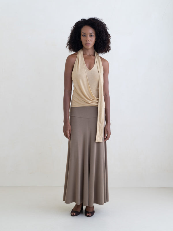 Woman wearing a light yellow sleeveless halter-style wrap top and a taupe maxi skirt on a white background. 