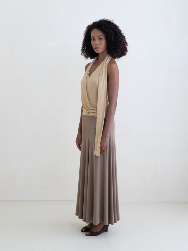 Woman wearing a light yellow sleeveless halter-style wrap top and a taupe maxi skirt on a white background. 
