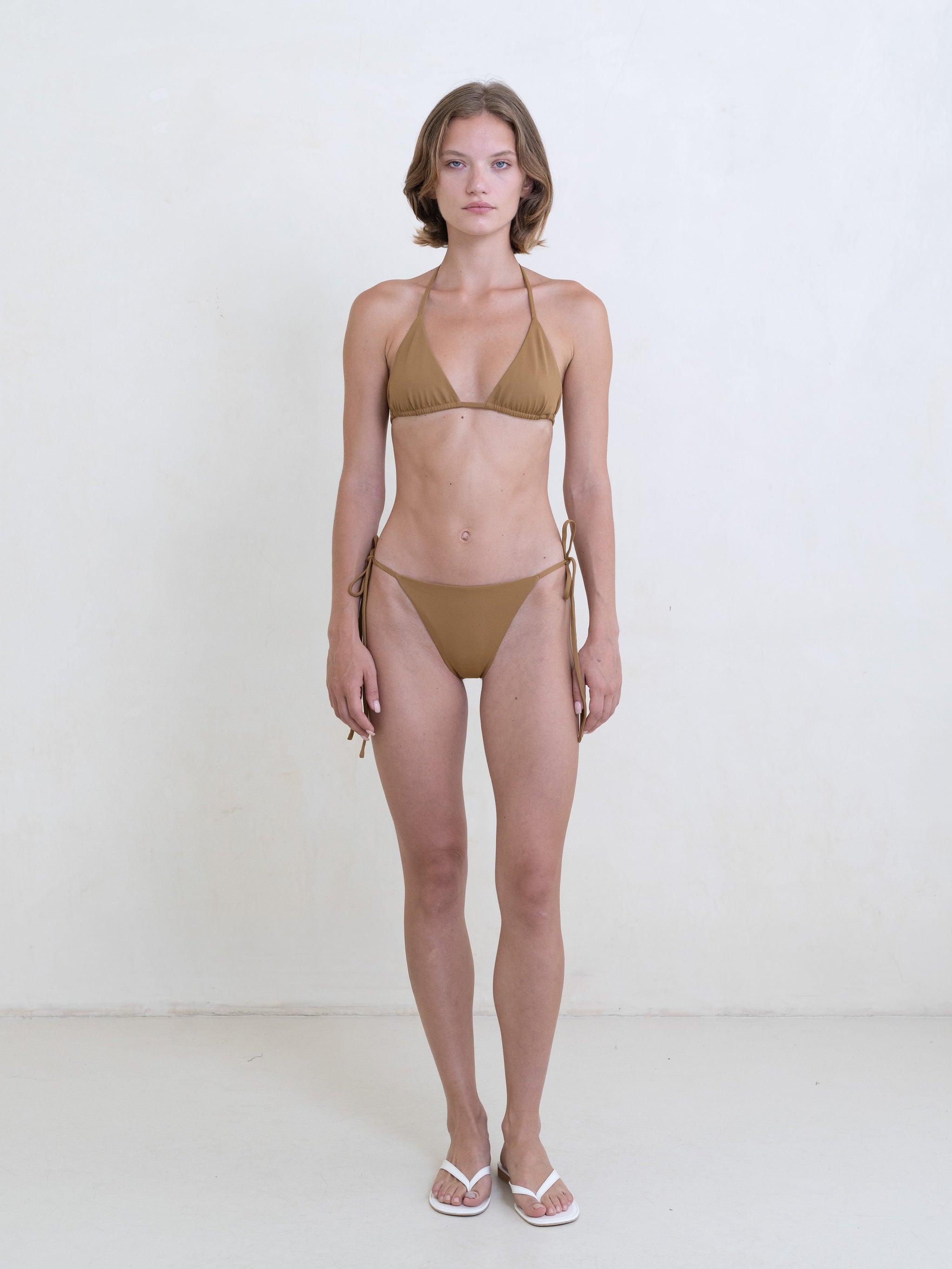 Woman wearing a golden brown bikini on a white background.