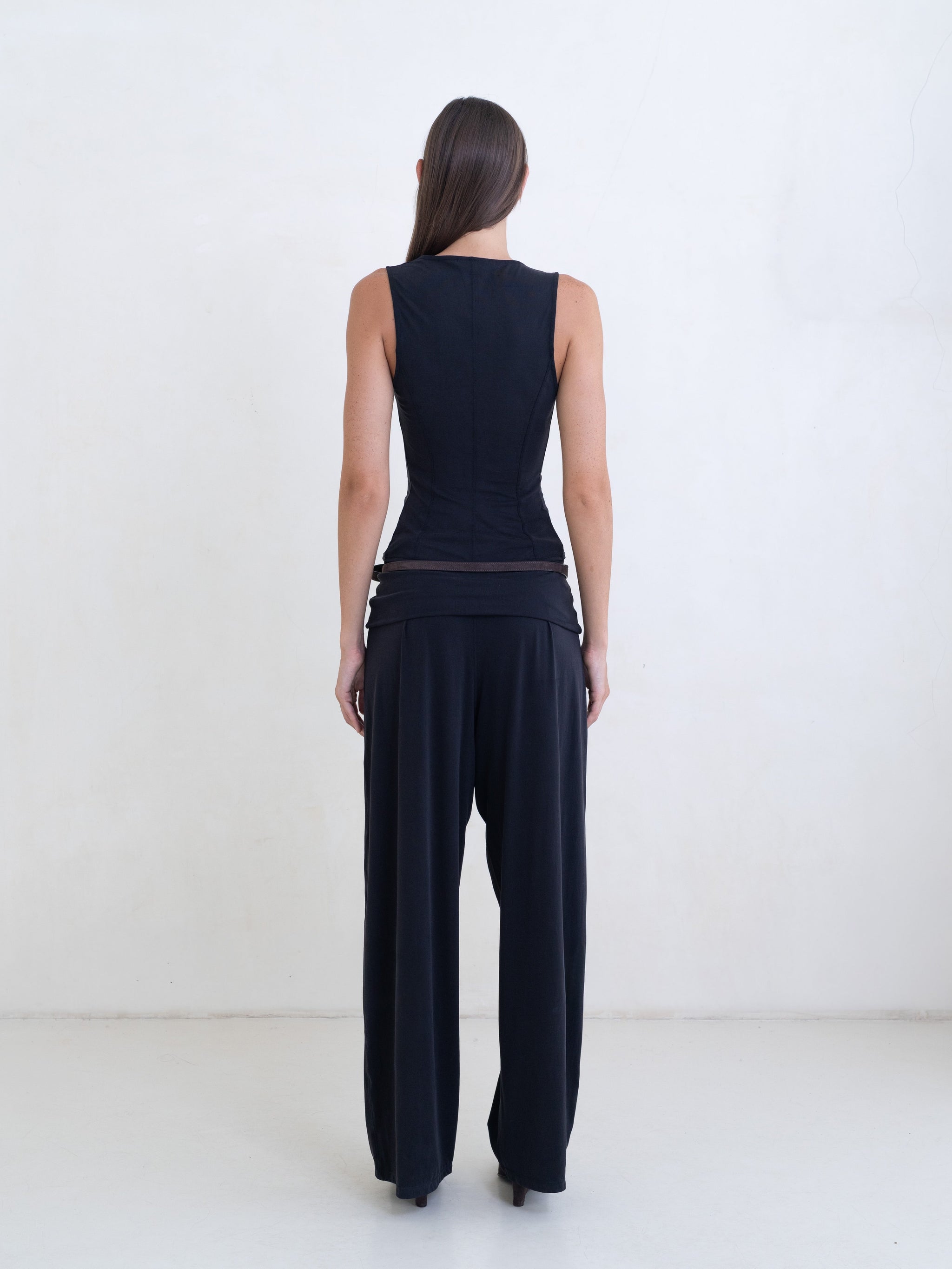 Woman wearing a black sleeveless cowl neck top and black pants on a white background. 
