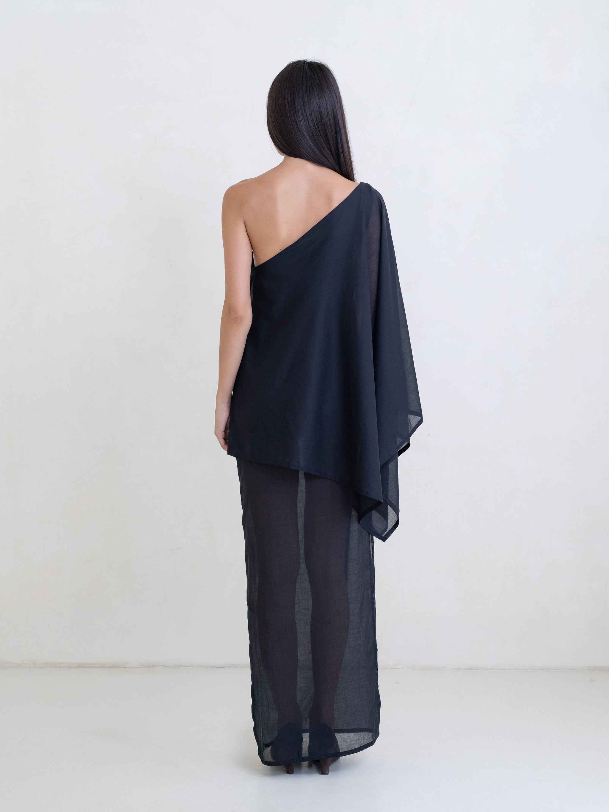 Woman wearing a black asymmetric maxi dress on a white background. 