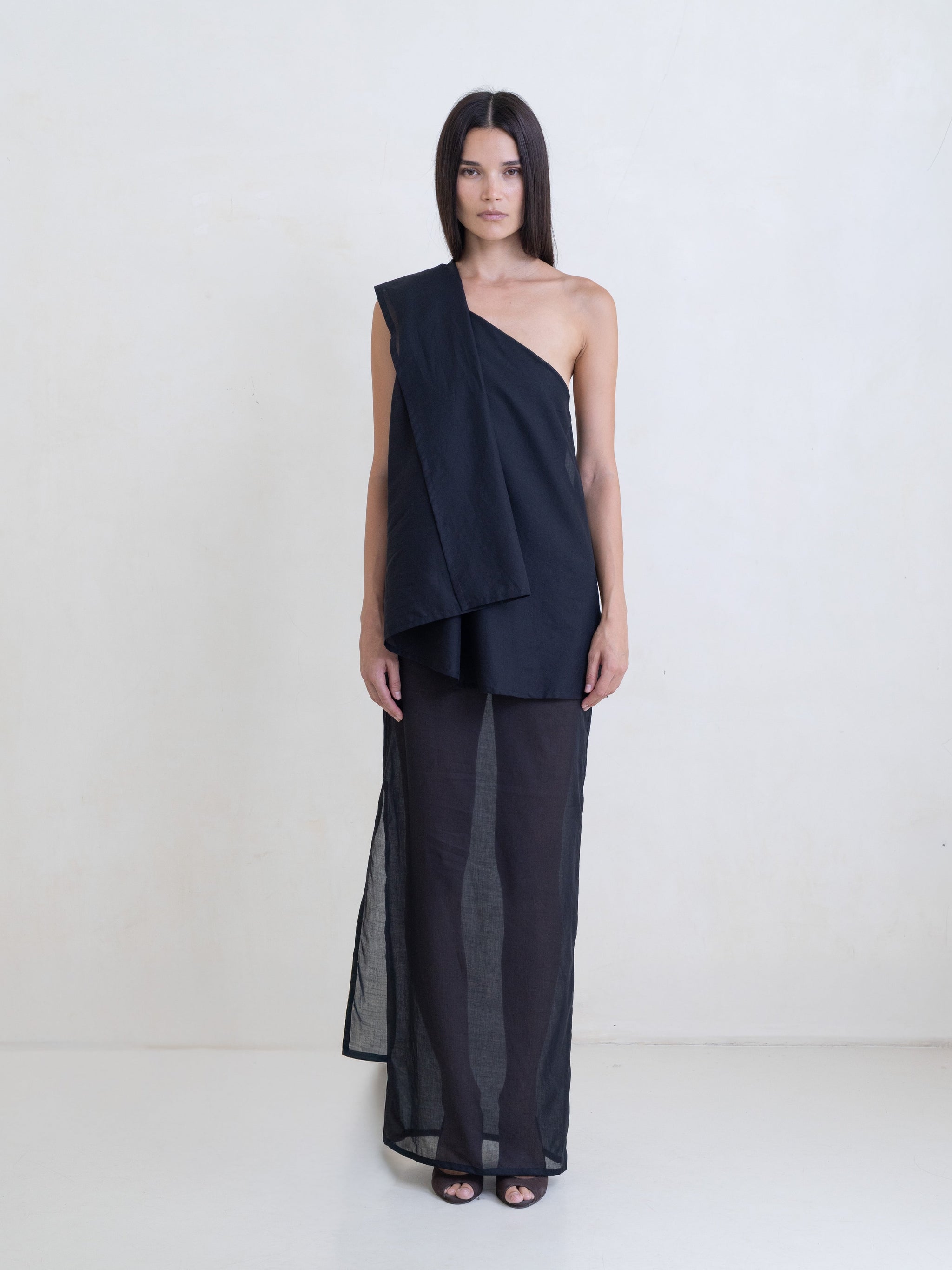 Woman wearing a black asymmetric maxi dress on a white background. 