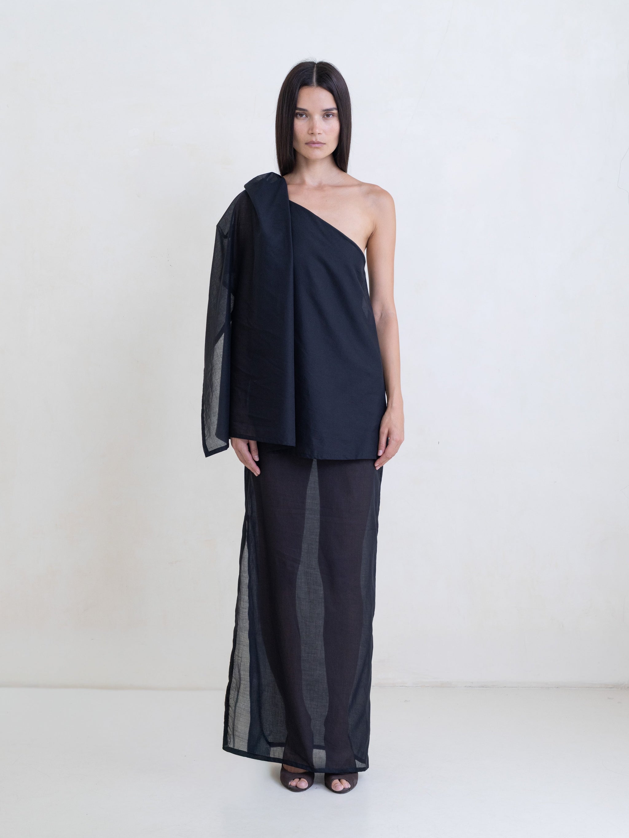 Woman wearing a black asymmetric maxi dress on a white background. 