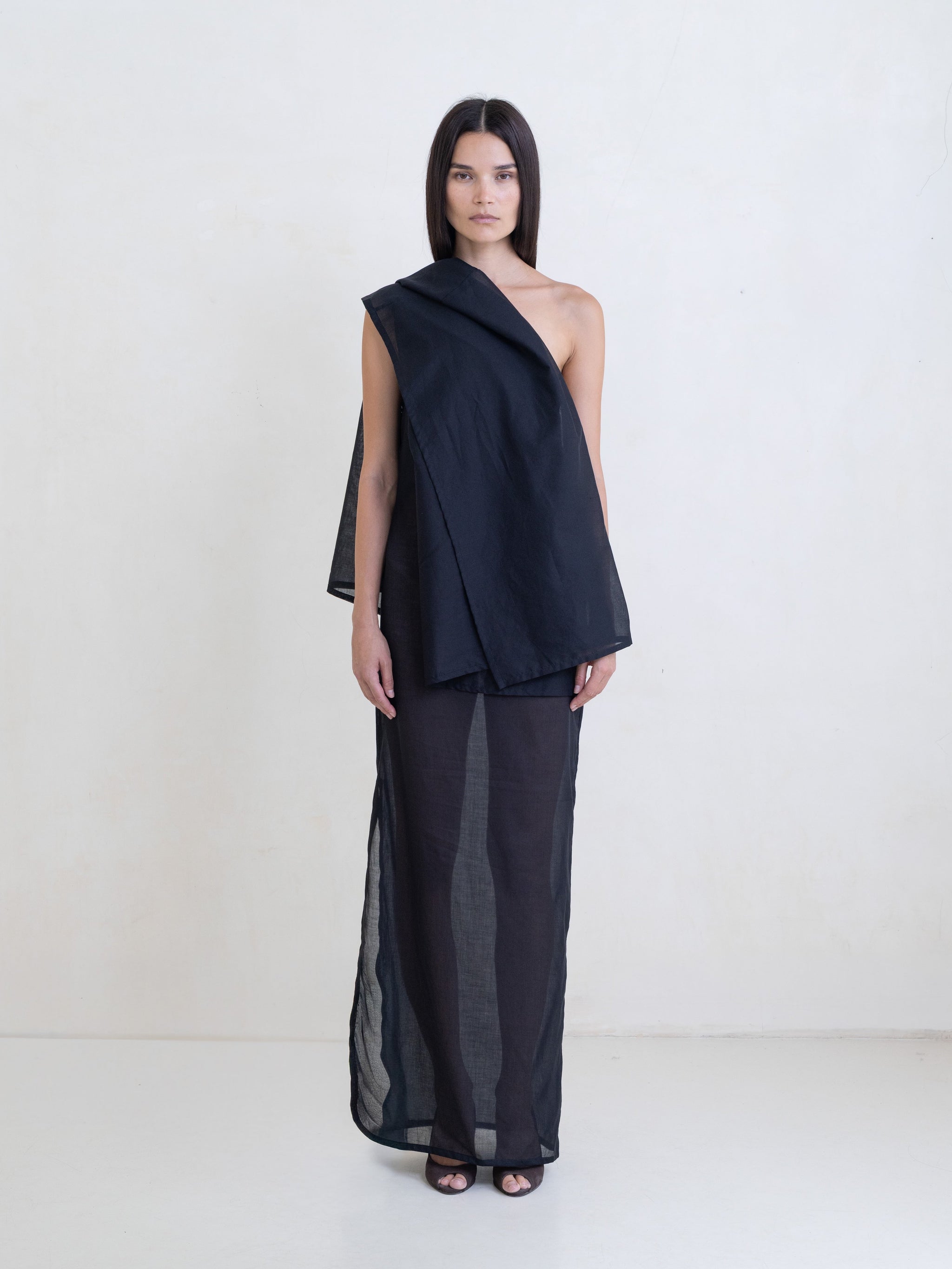 Woman wearing a black asymmetric maxi dress on a white background. 