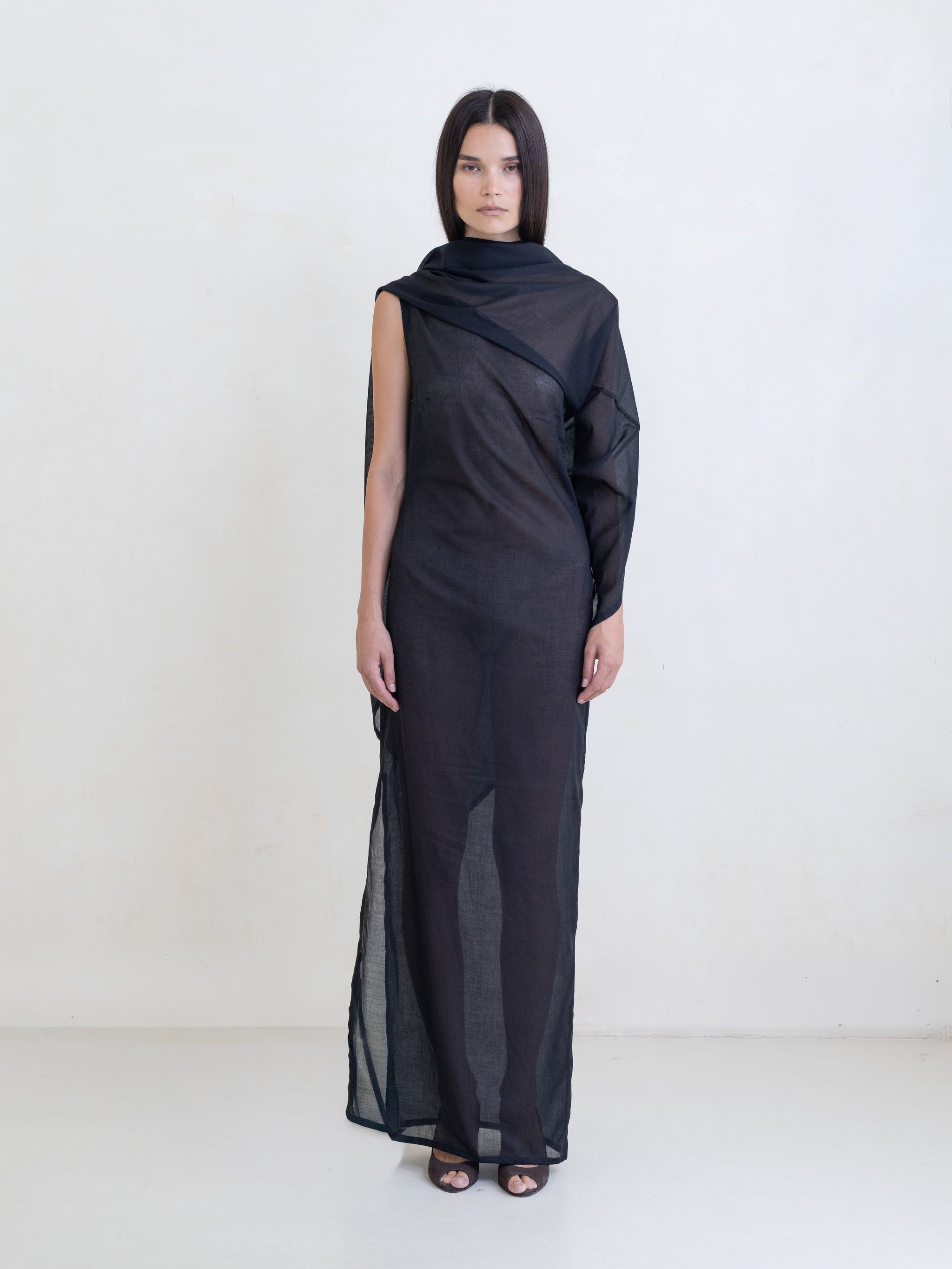 Woman wearing a black asymmetric maxi dress on a white background. 
