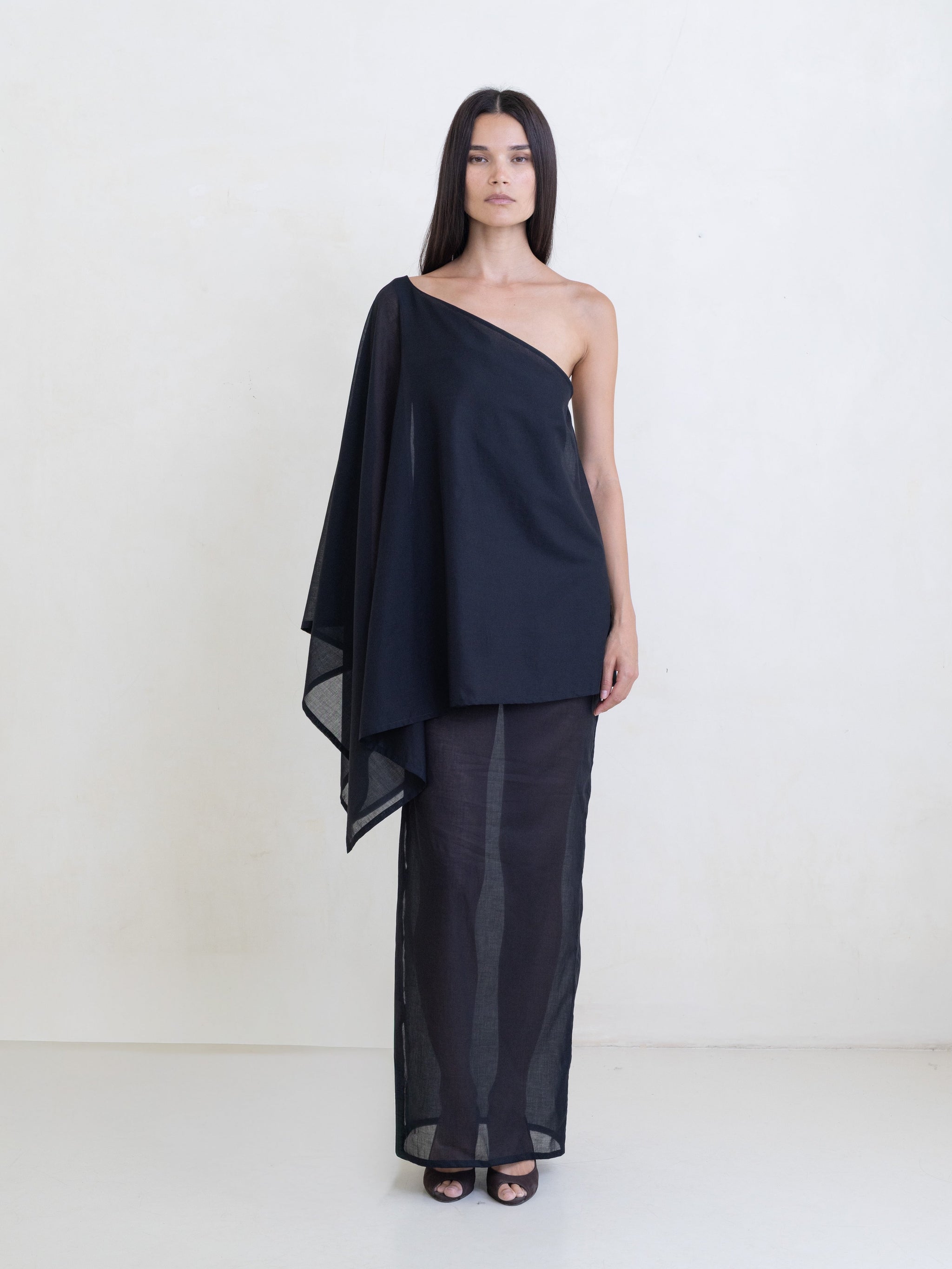 Woman wearing a black asymmetric maxi dress on a white background. 