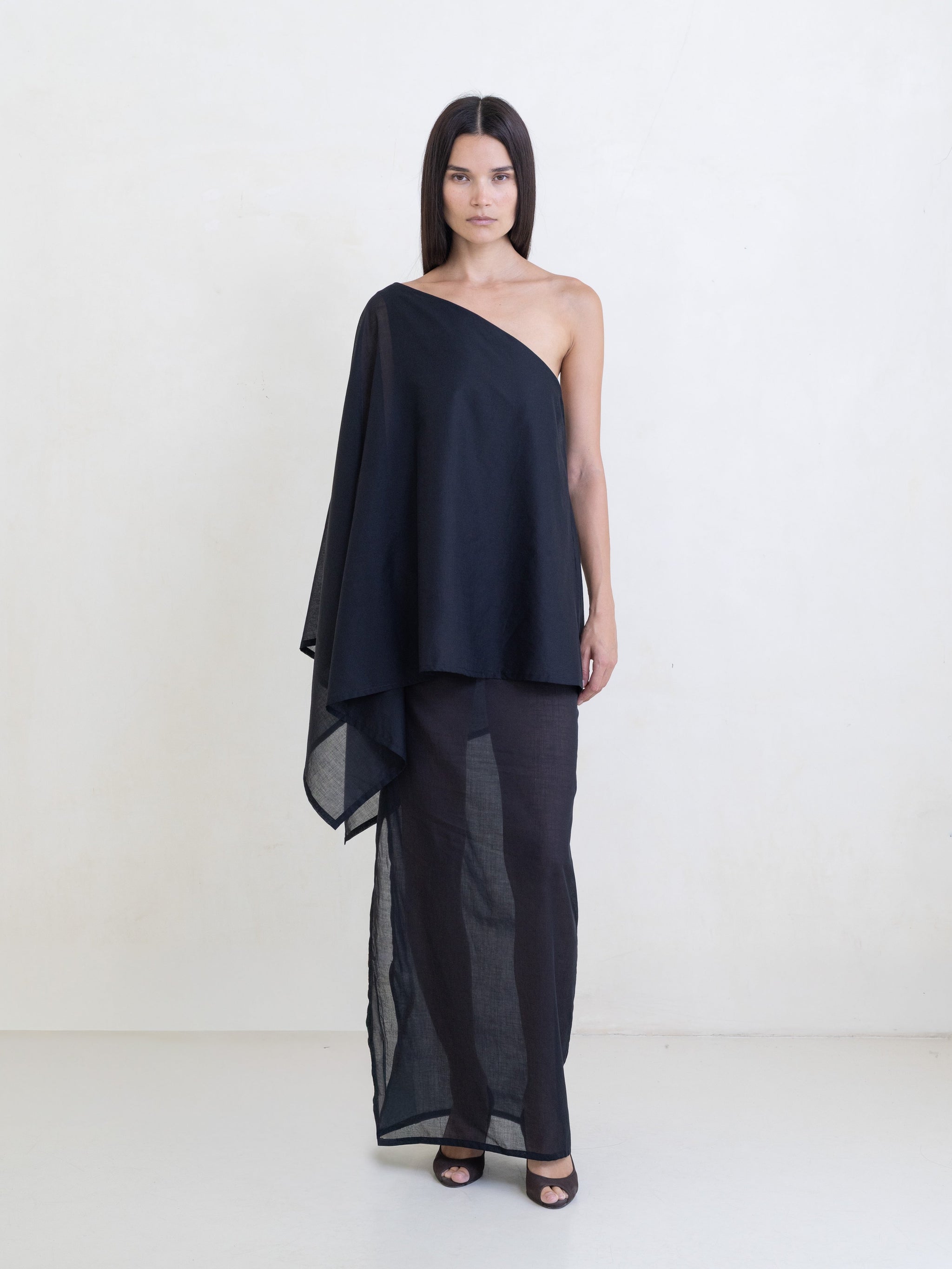 Woman wearing a black asymmetric maxi dress on a white background. 