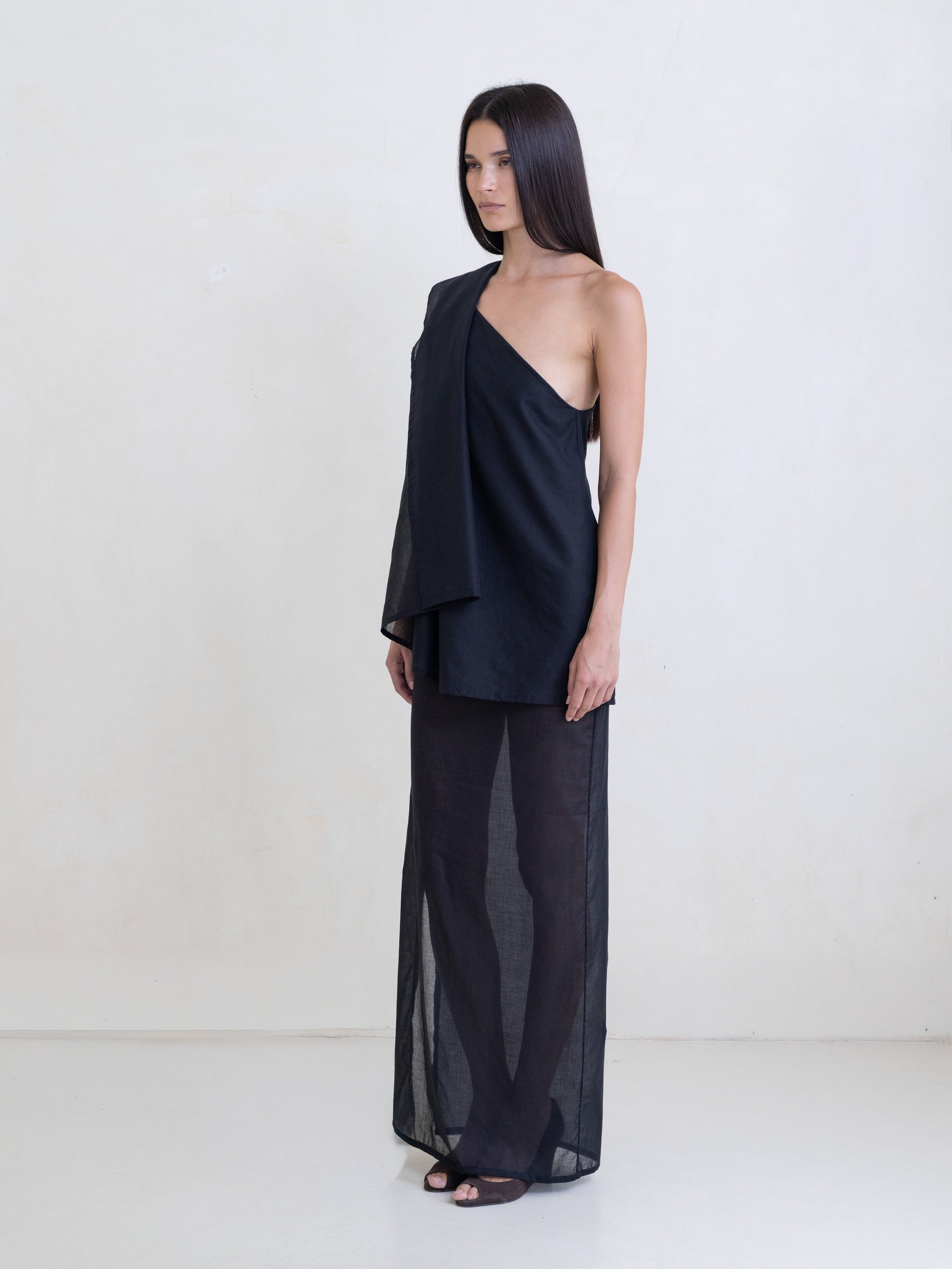 Woman wearing a black asymmetric maxi dress on a white background. 