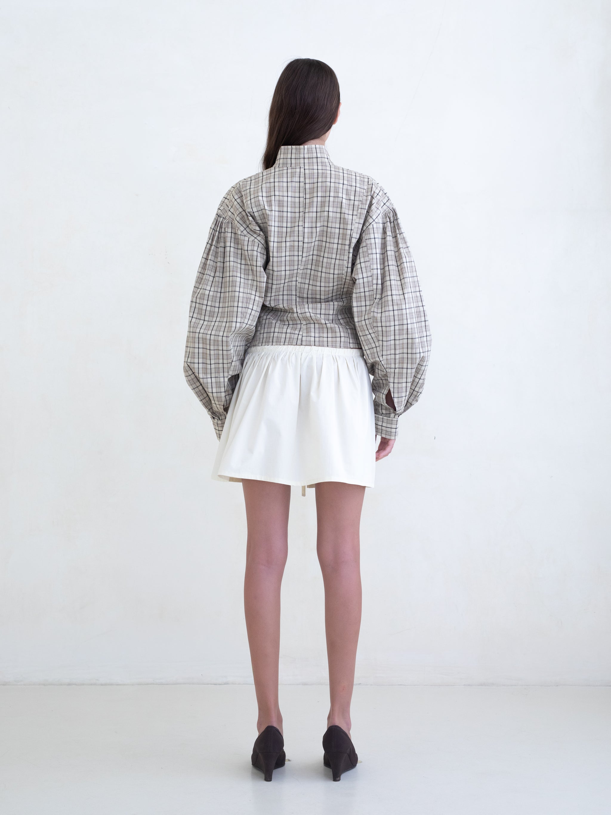 Woman wearing a brown plaid zip-front jacket and a cream mini skirt on a white background. 